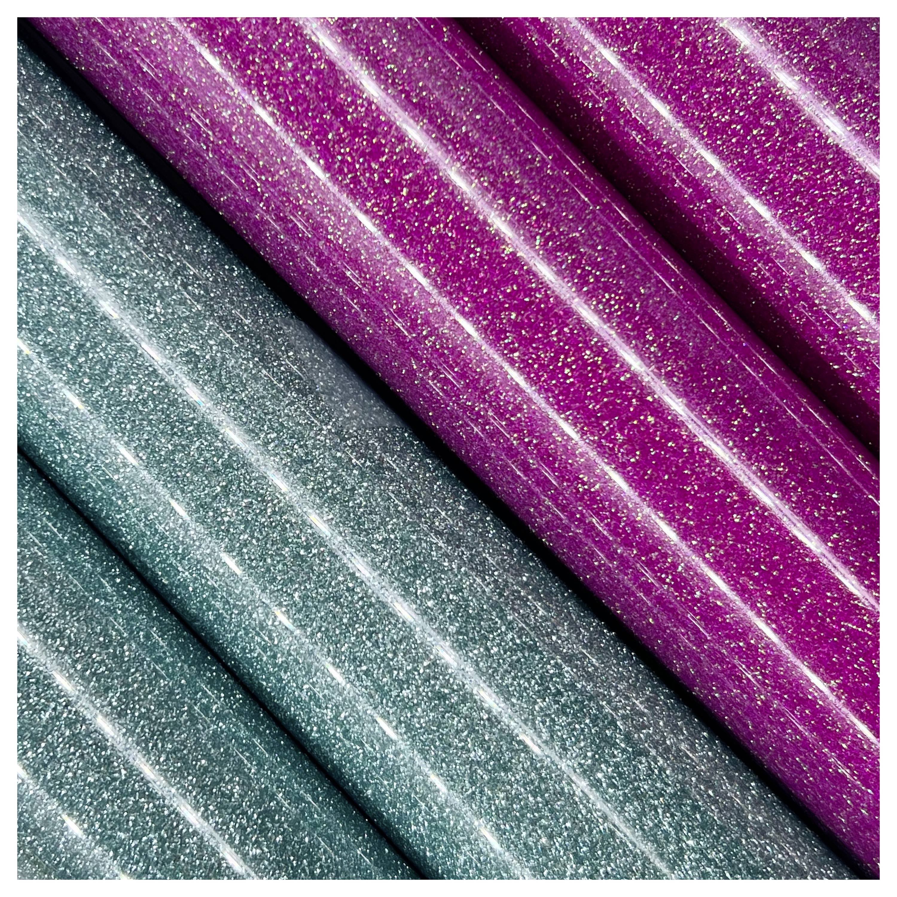 Nahaufnahme von glitzernden Glitterpapirrollen, mit drei Rollen in Blaugrün und zwei Rollen in Magenta, die eine schimmernde Textur und Farbkontrast zeigen.