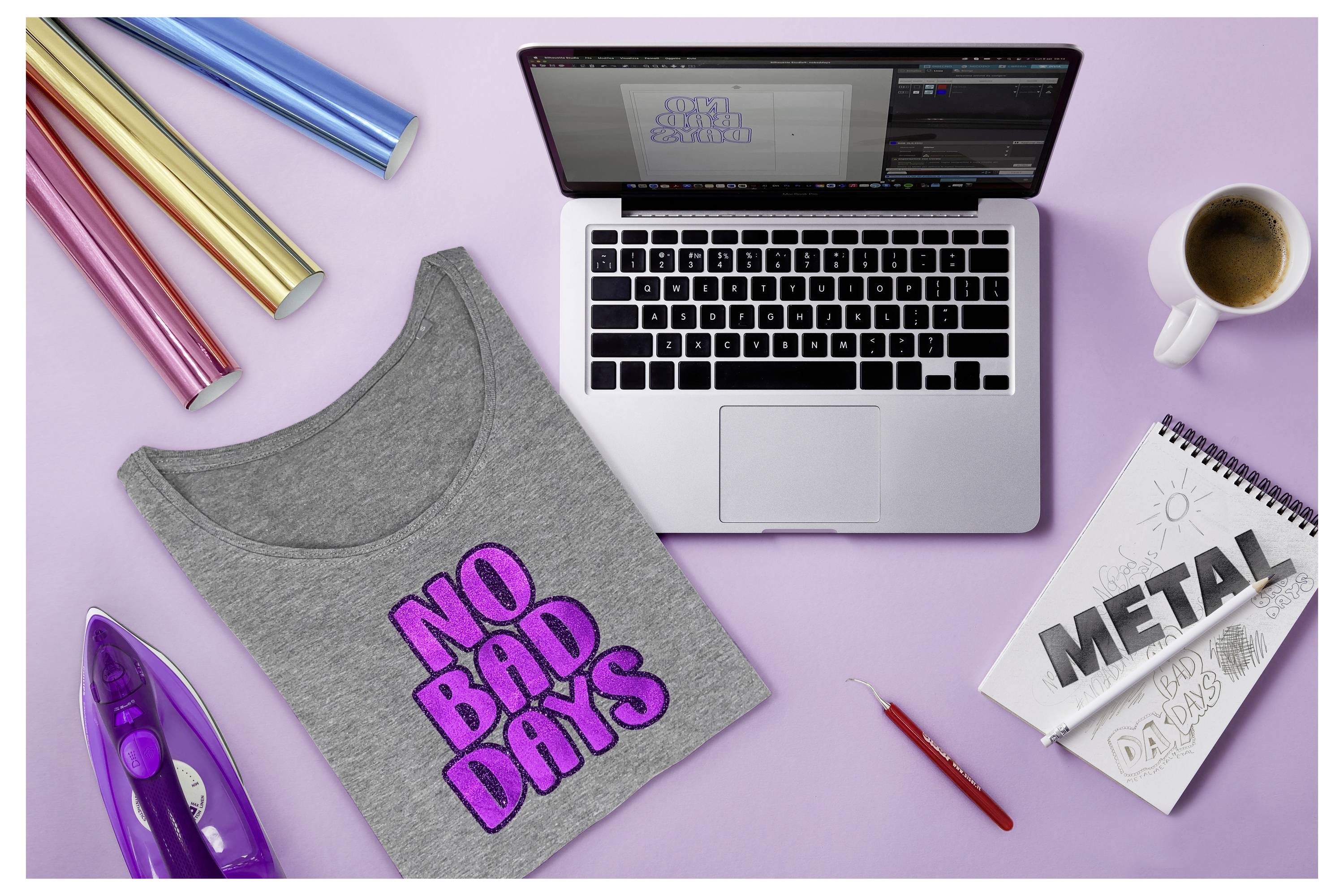 Ein Laptop, auf dem Grafiksoftware angezeigt wird, Bügeldesign-Materialien, ein Bügeleisen und Papier mit dem Text „METAL
