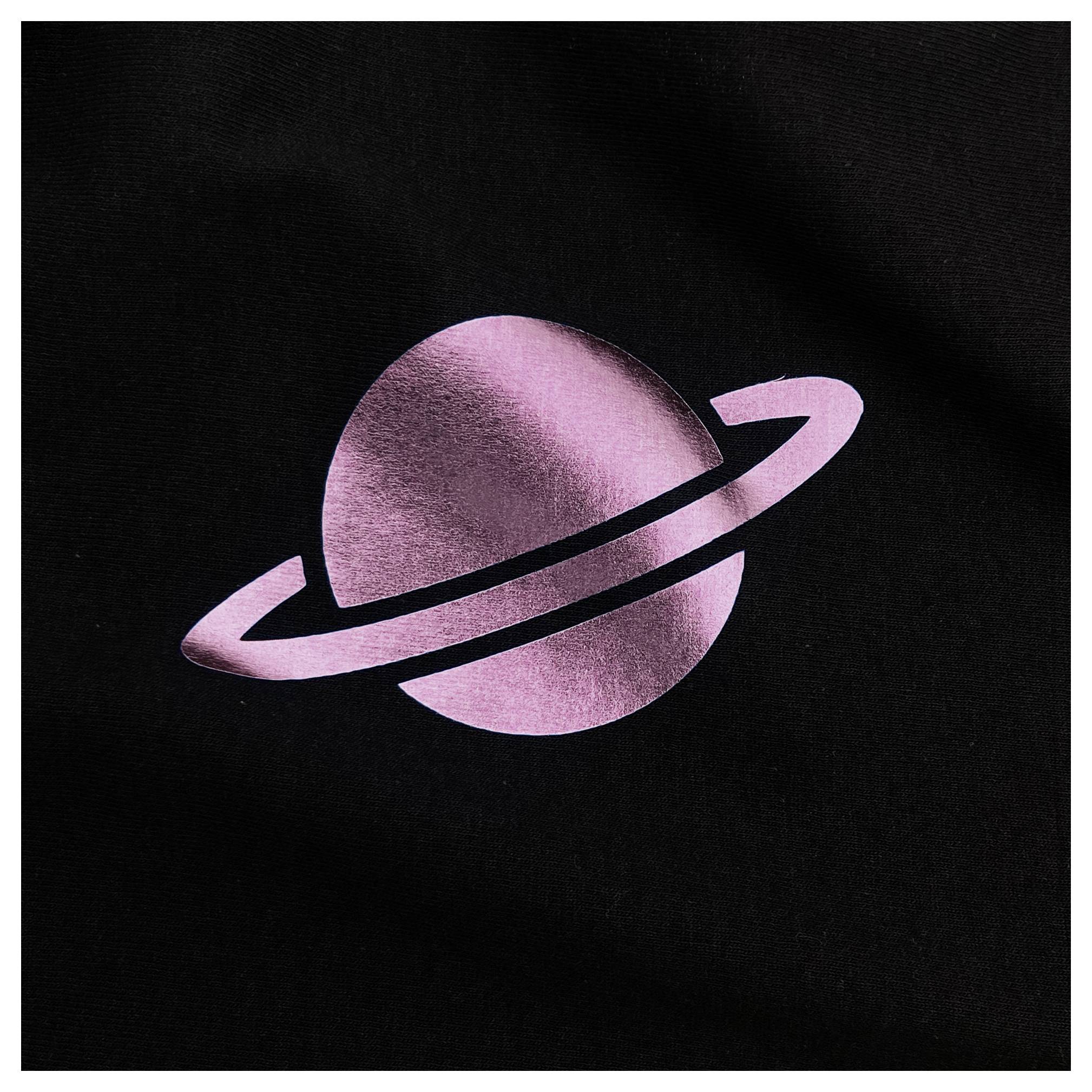 Ein rosafarbener metallischer Planet mit einem Ring vor schwarzem Hintergrund.