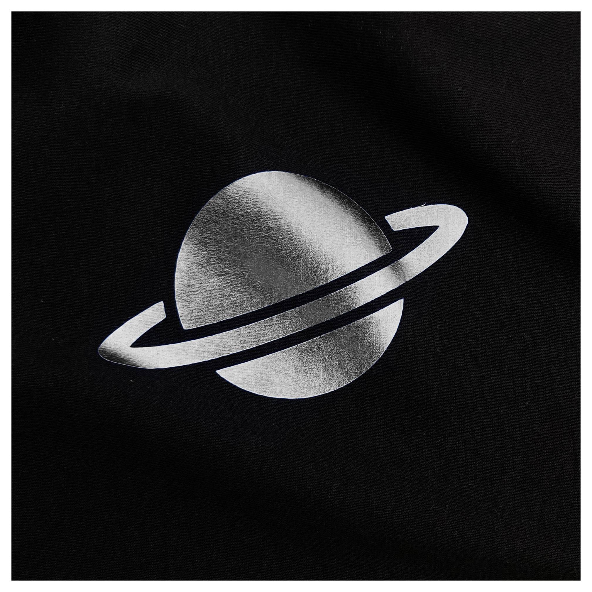 Eine metallische silberne Darstellung eines Planeten mit Ringen auf schwarzem Hintergrund, ähnlich dem Saturn.