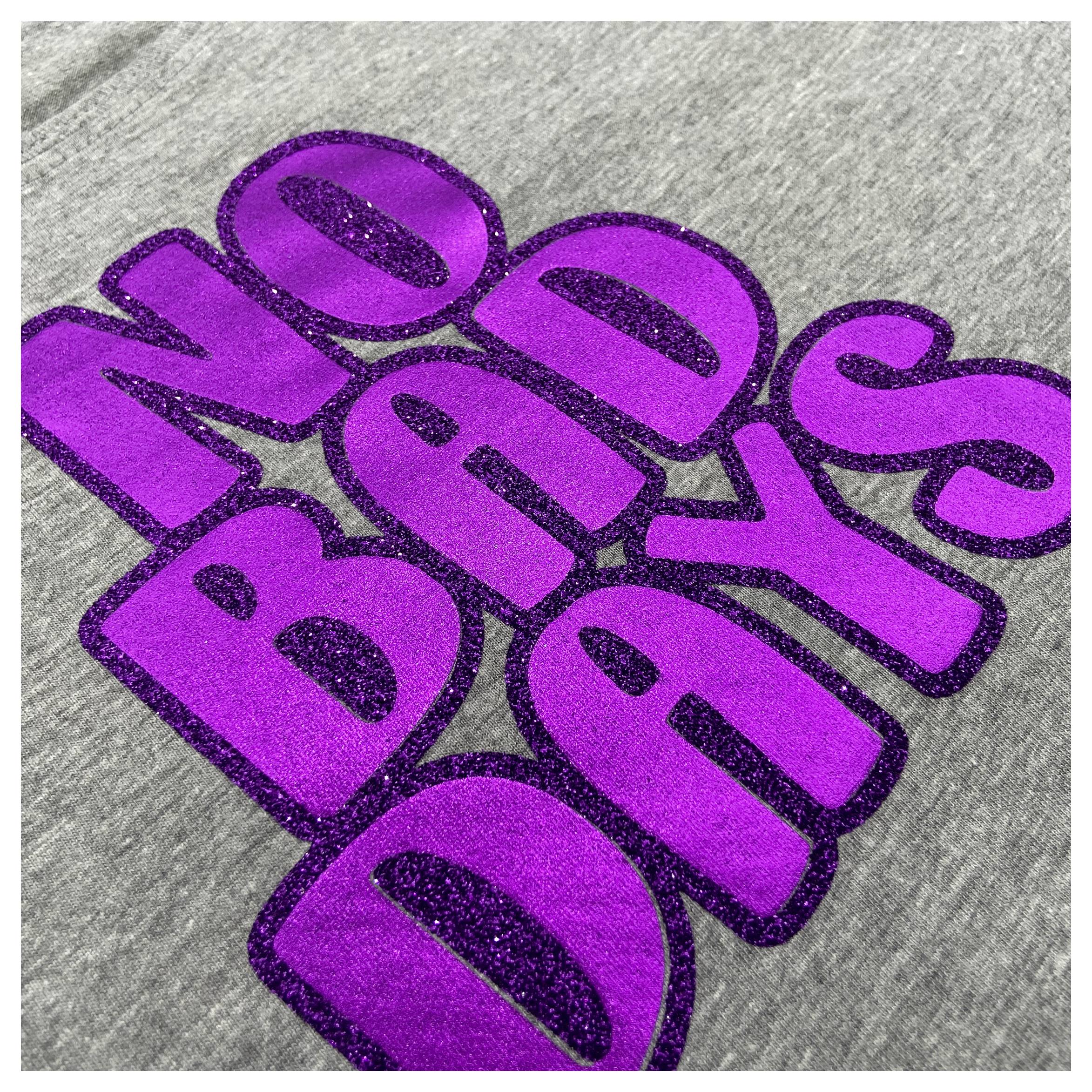 Das Bild zeigt einen grauen Stoff mit kühnem, violettem glitzerndem Text mit der Aufschrift 