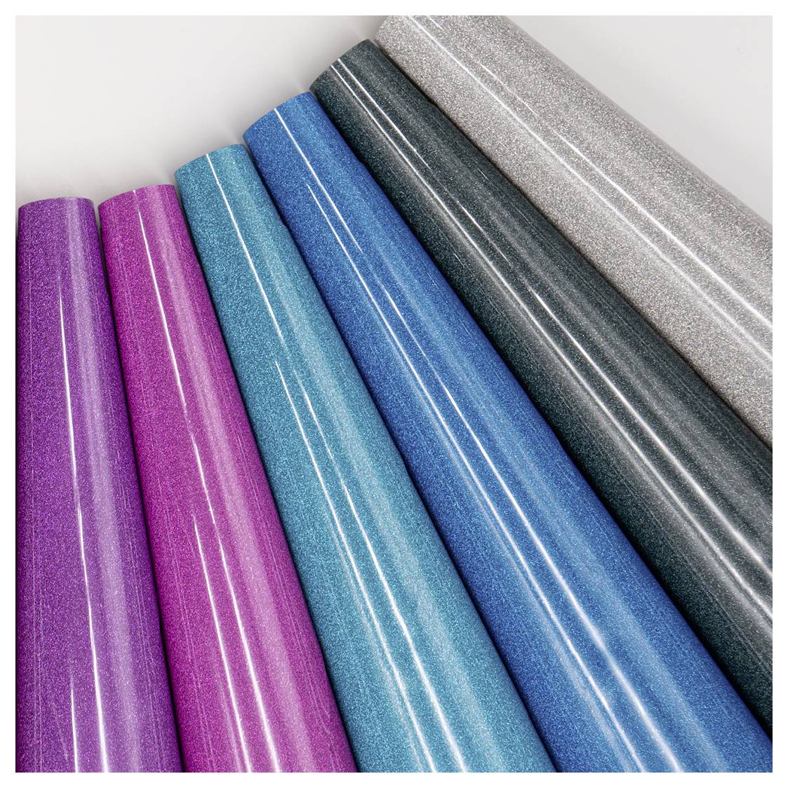 Glänzende Vinylrollen in verschiedenen Farben, darunter Lila, Rosa, Türkis, Blau, Silber und Schwarz, diagonal angeordnet.