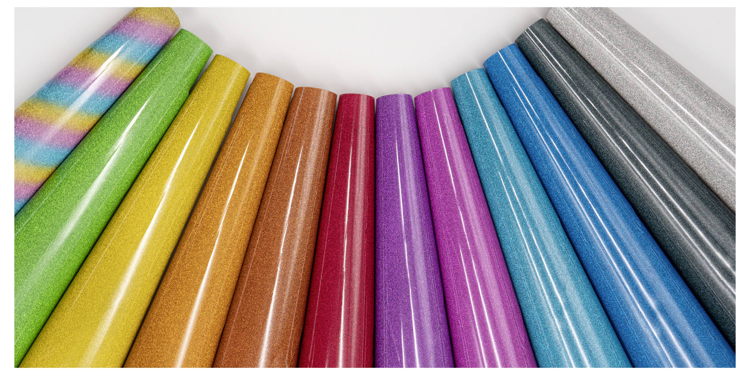 Farbenfrohe Rollen Geschenkpapier in Fächerform angeordnet, mit verschiedenen Mustern und Farbtönen, einschließlich Regenbogen, Volltonfarben und Glitter.