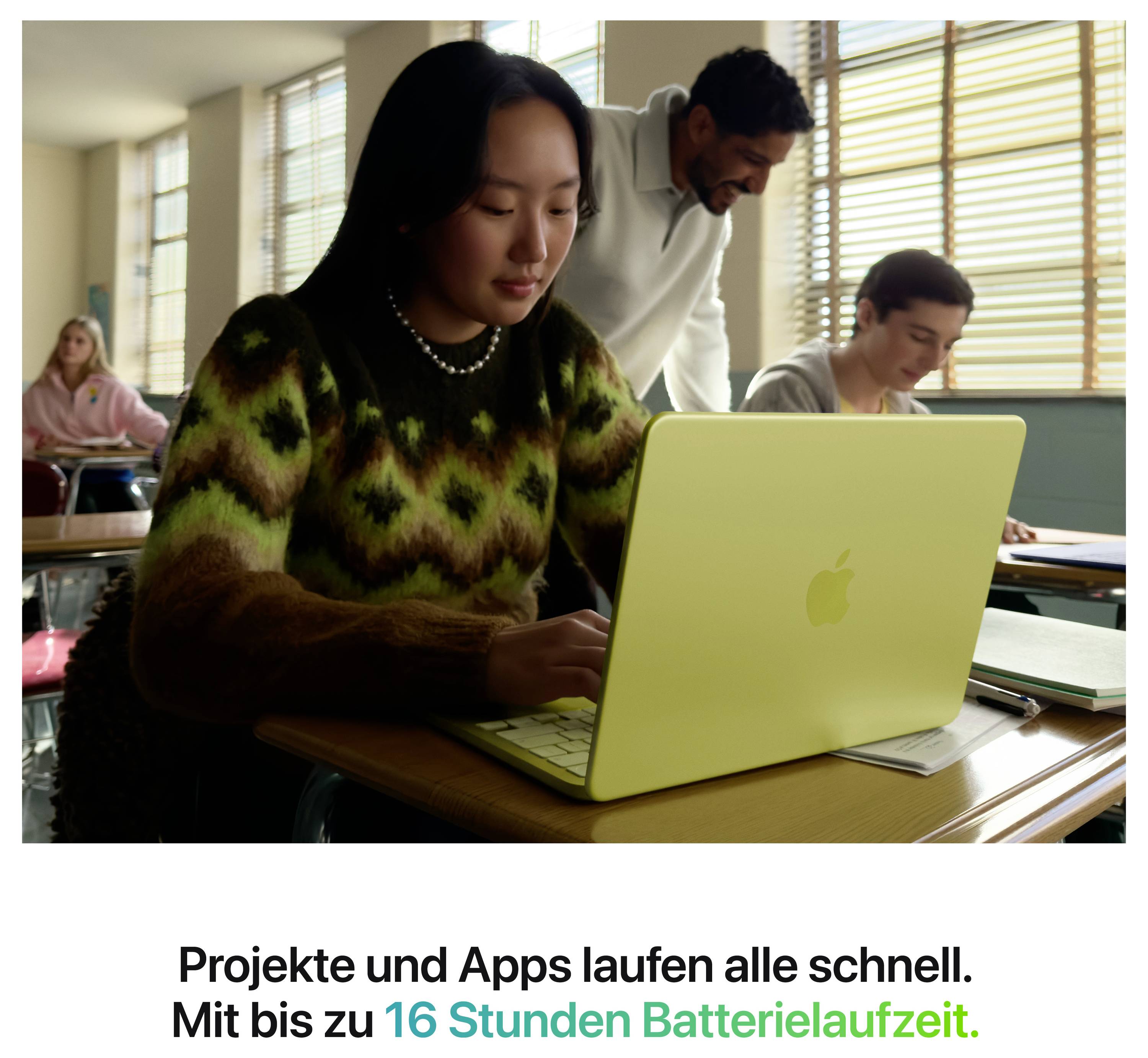 Eine Frau sitzt in einem Klassenraum und arbeitet an einem gelben Laptop, daneben stehen zwei Personen. Der Text hebt eine Batterielaufzeit von bis zu 16 Stunden hervor.