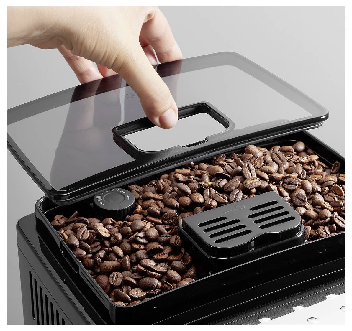 Eine Hand öffnet eine Kaffeebohnenmühle, die mit gerösteten Kaffeebohnen gefüllt ist, und zeigt die Textur der Bohnen und den abnehmbaren Deckel der Mühle.