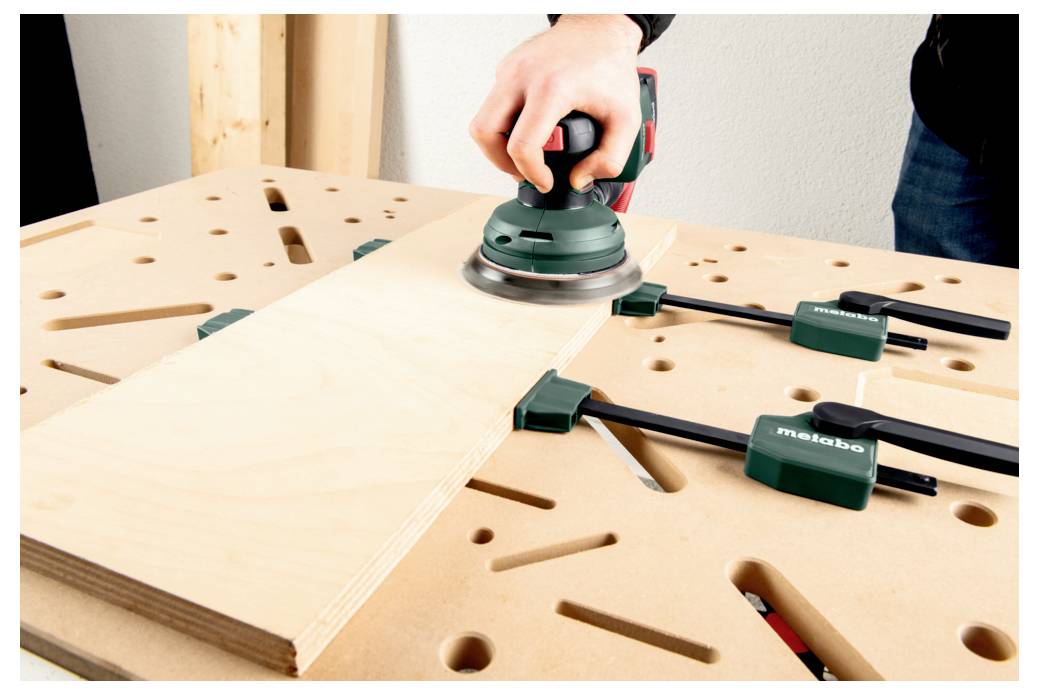 Eine grüne und silberne Schraubzwinge sichert zwei Holzstücke auf einer Werkbank und zeigt die Verwendung eines Holzbearbeitungswerkzeugs.