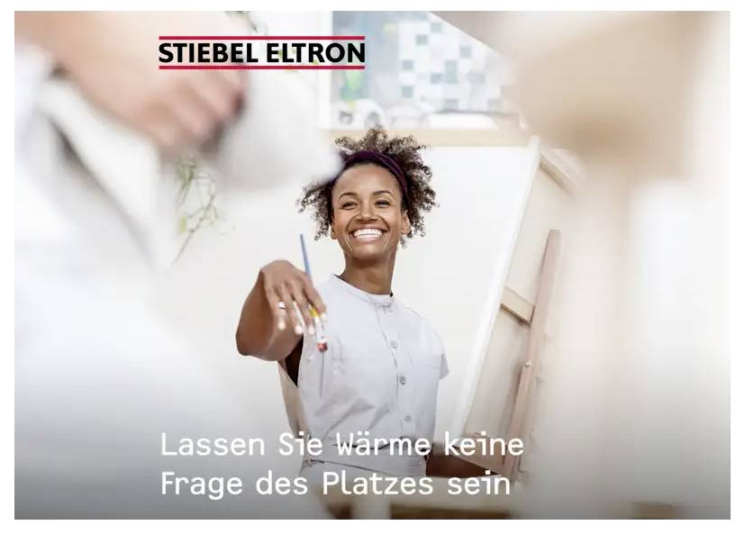 Eine lächelnde Person im weißen Hemd hält einen Pinsel. Der Text lautet: Lassen Sie Wärme keine Frage des Platzes sein mit dem Logo „STIEBEL ELTRON
