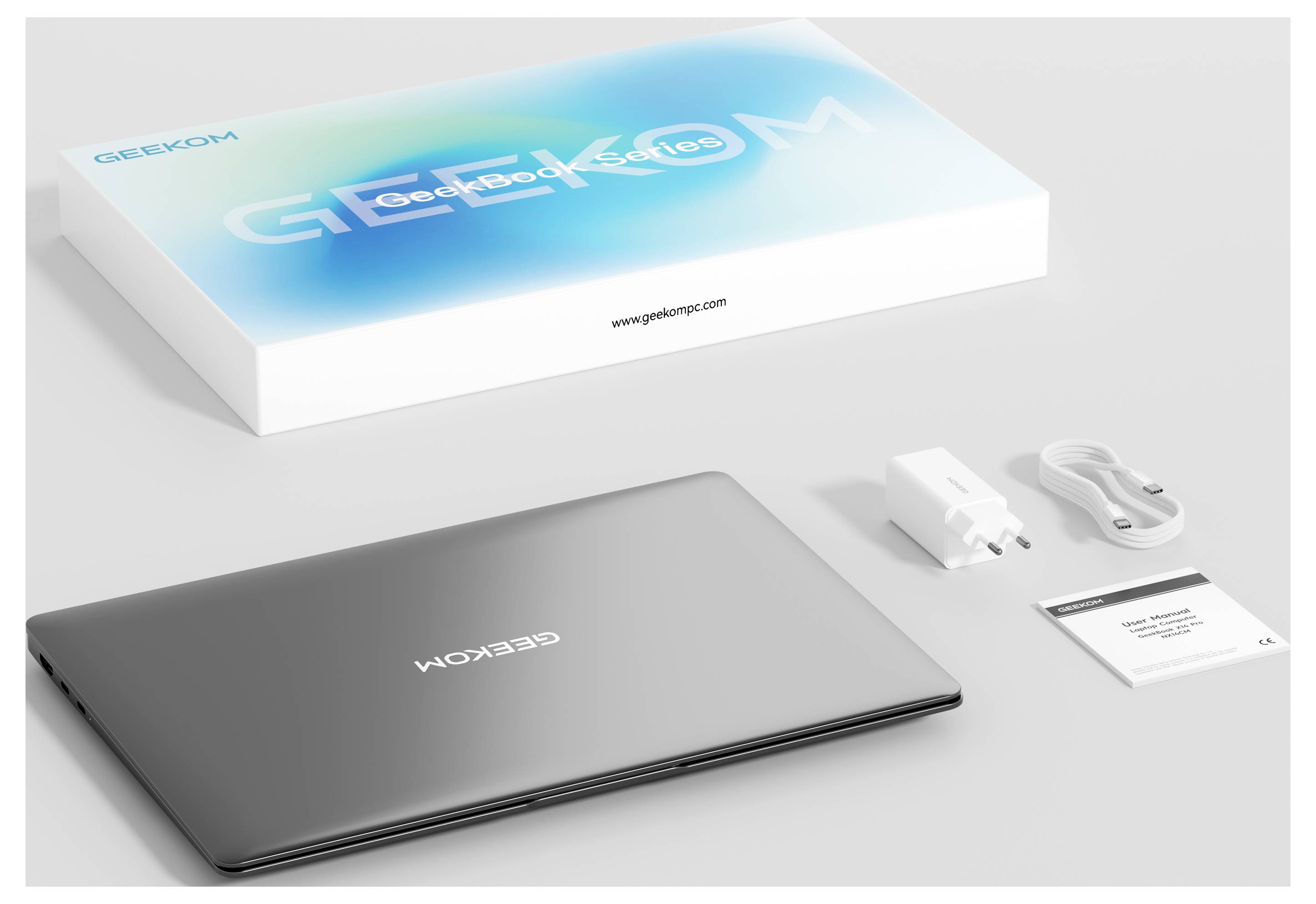 Ein verpacktes Laptop-Set, das einen geschlossenen Laptop, ein Ladegerät, ein Kabel, eine Bedienungsanleitung und eine Verpackung mit „Geekom