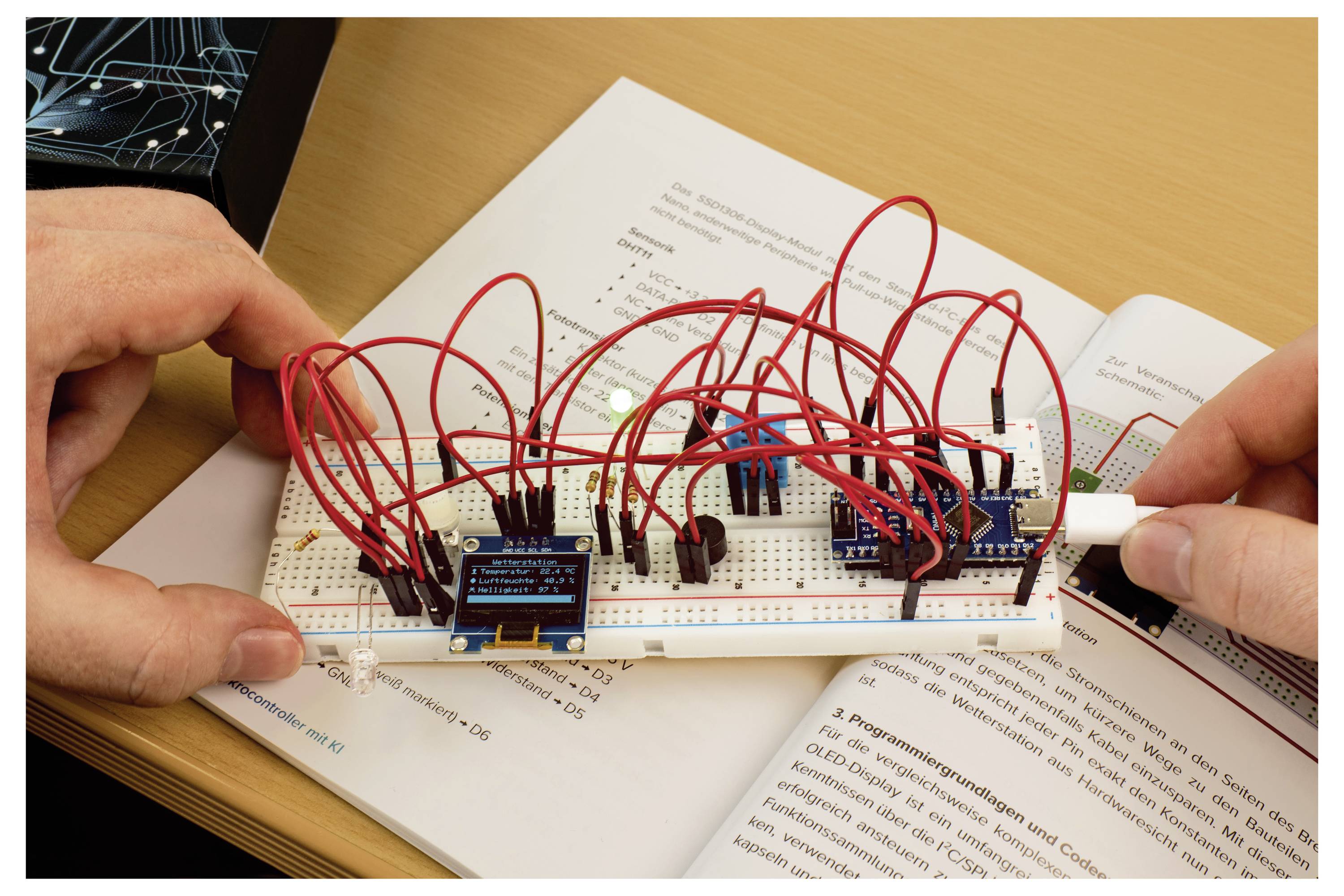 Eine Person verbindet rote Drähte auf einem Steckbrett mit verschiedenen elektronischen Komponenten über einem offenen Lehrbuch und demonstriert ein Schaltungsaufbau.