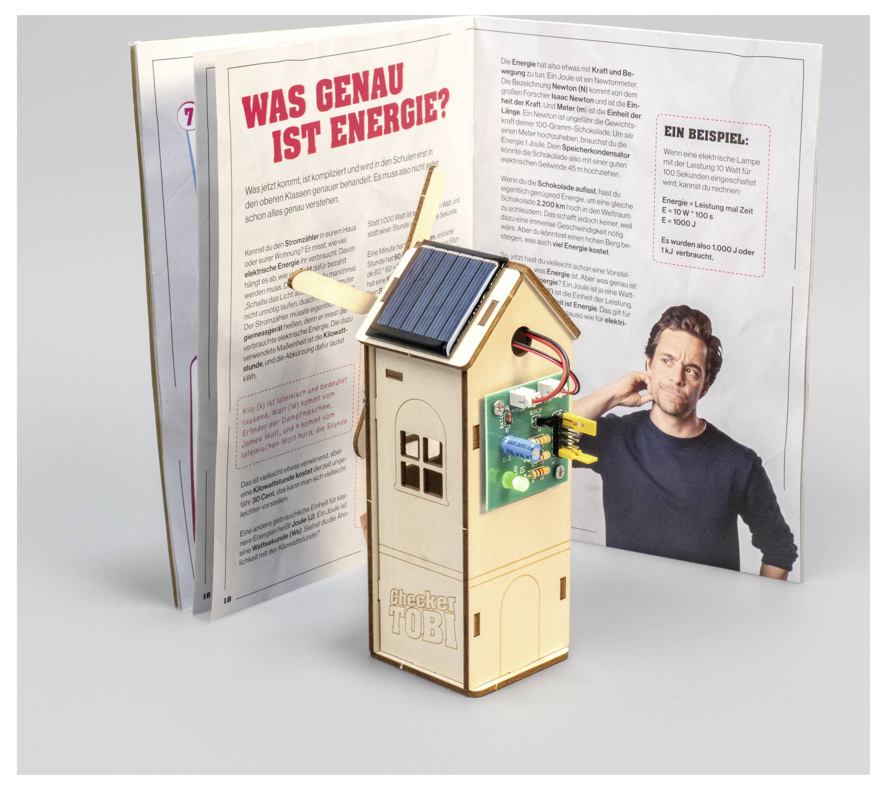 Ein hölzernes Modell mit einem Solarpanel und einer Leiterplatte steht vor einem aufgeschlagenen Buch mit dem Titel „Was genau ist Energie?