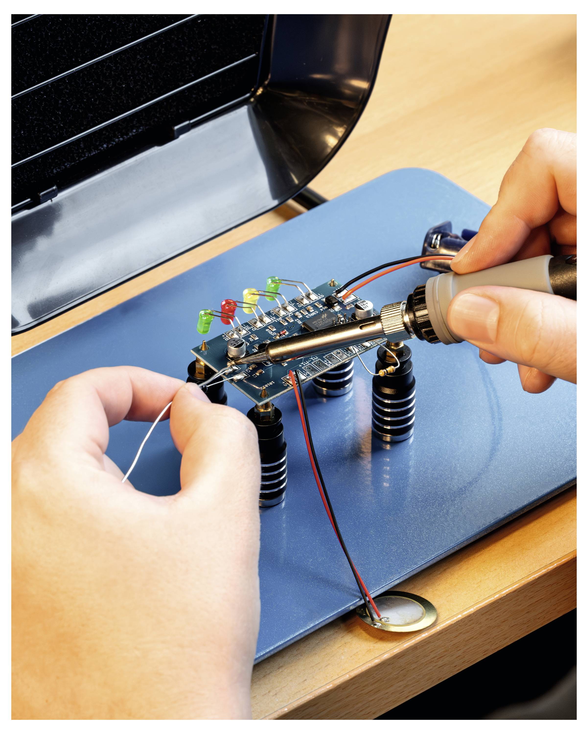 Hände löten Komponenten auf einer kleinen elektronischen Leiterplatte mit verschiedenen LEDs und Drähten.