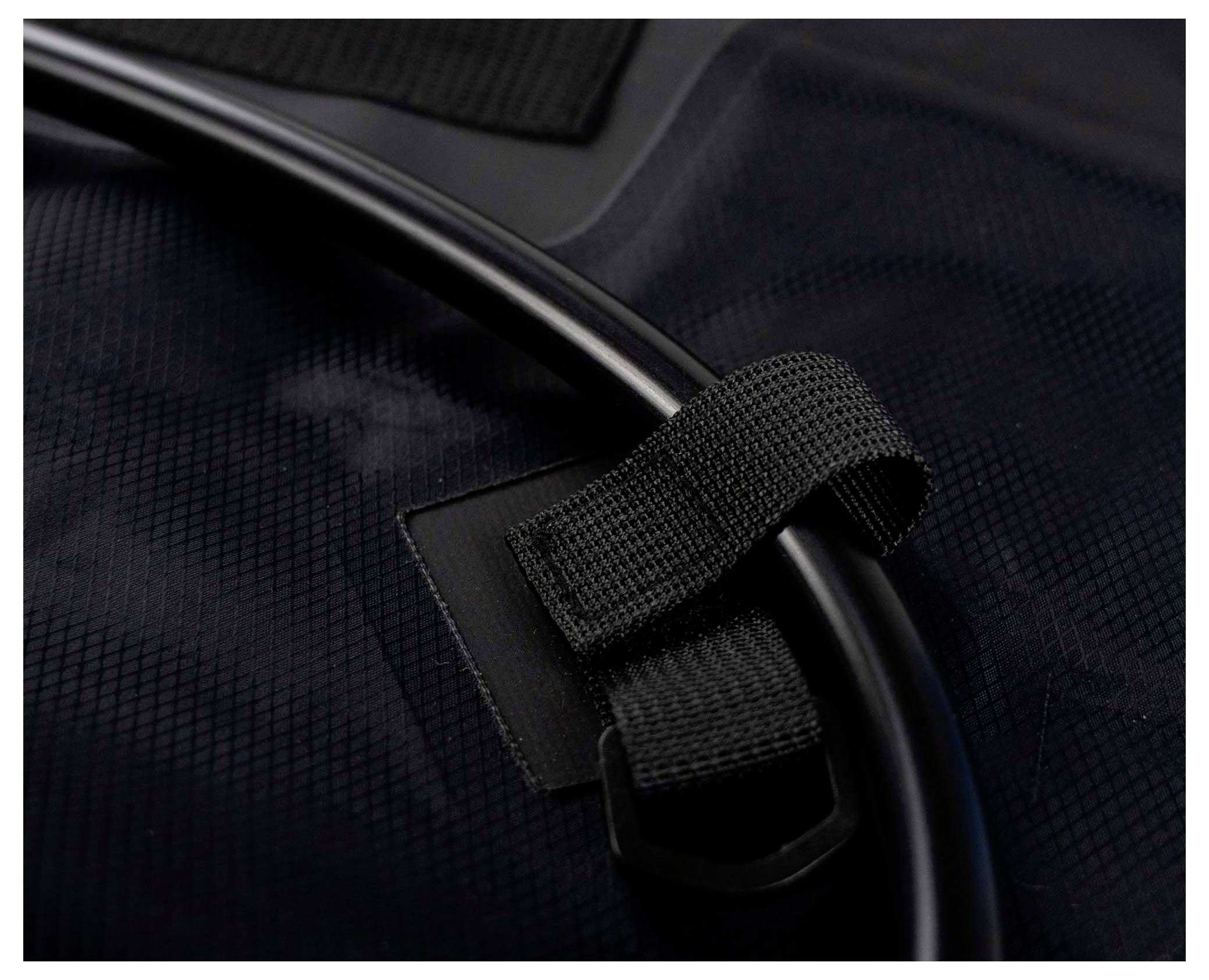 Eine Nahaufnahme eines schwarzen Stoffriemens und einer schwarzen Schlaufe, die einen schwarzen Schlauch sichern, was auf eine kompakte und organisierte Anordnung oder Aufbewahrungslösung hindeutet.