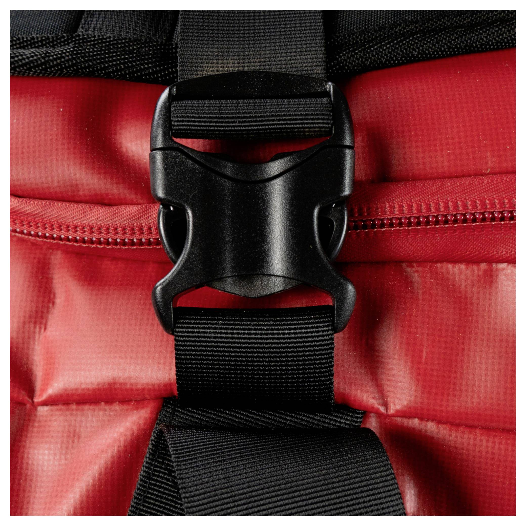 Eine Nahaufnahme eines roten Rucksacks mit einer schwarzen Schnalle, die über einem Reißverschluss befestigt ist. Die Schnalle und der Riemen sind zentral positioniert und zeigen eine sichere Befestigung.