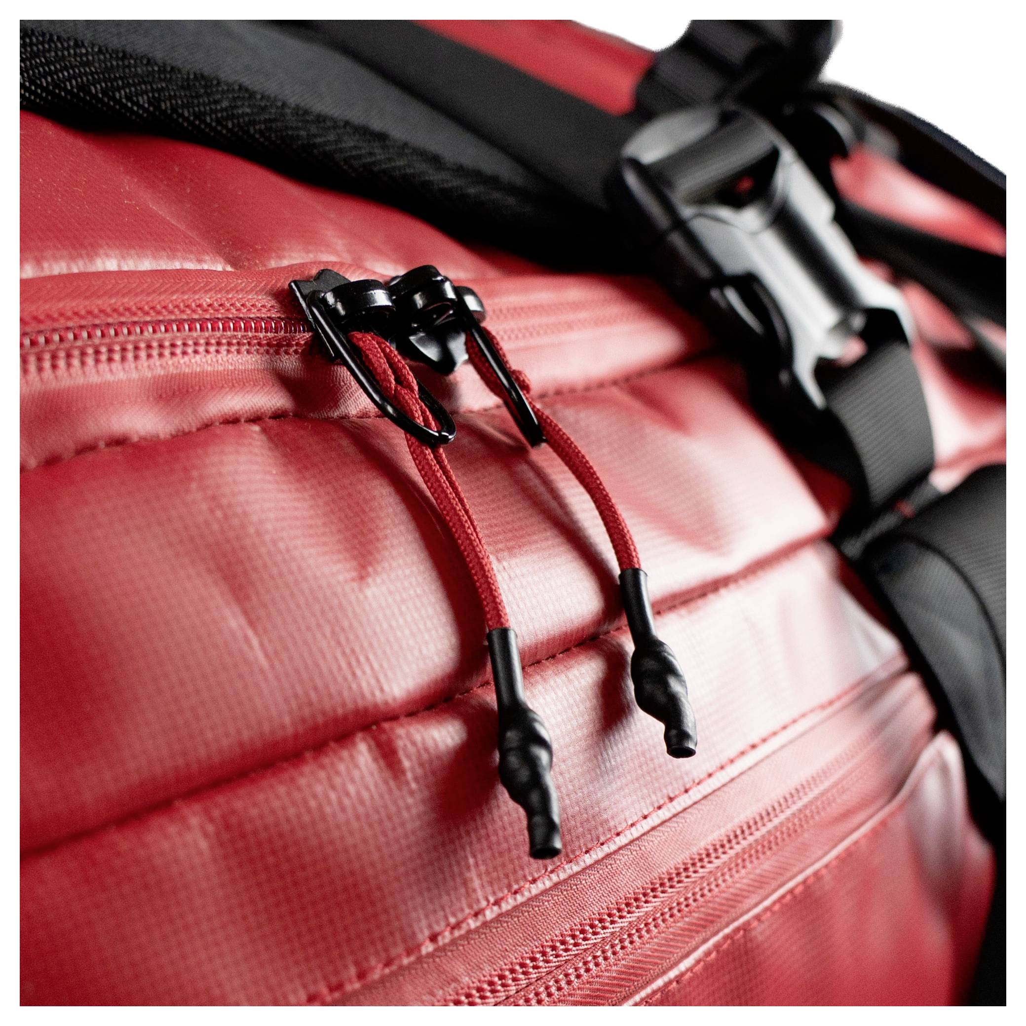 Ein Nahaufnahmebild, das eine rote Reisetasche mit zwei Reißverschlüssen und einem schwarzen Riemen zeigt. Der Fokus liegt auf dem robusten Material der Tasche und den Details der Reißverschlüsse.