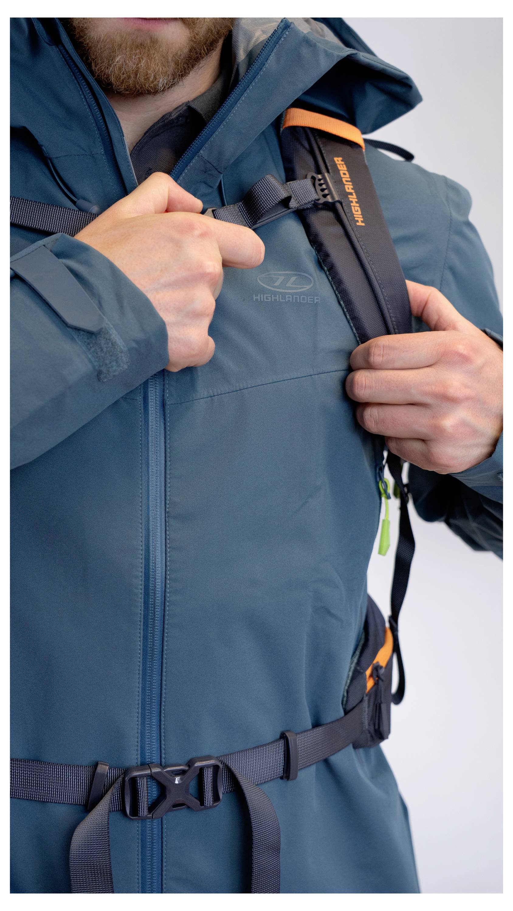 Eine Person stellt den Schultergurt einer blauen wasserdichten Jacke ein und signalisiert damit Bereitschaft für Outdoor-Aktivitäten.