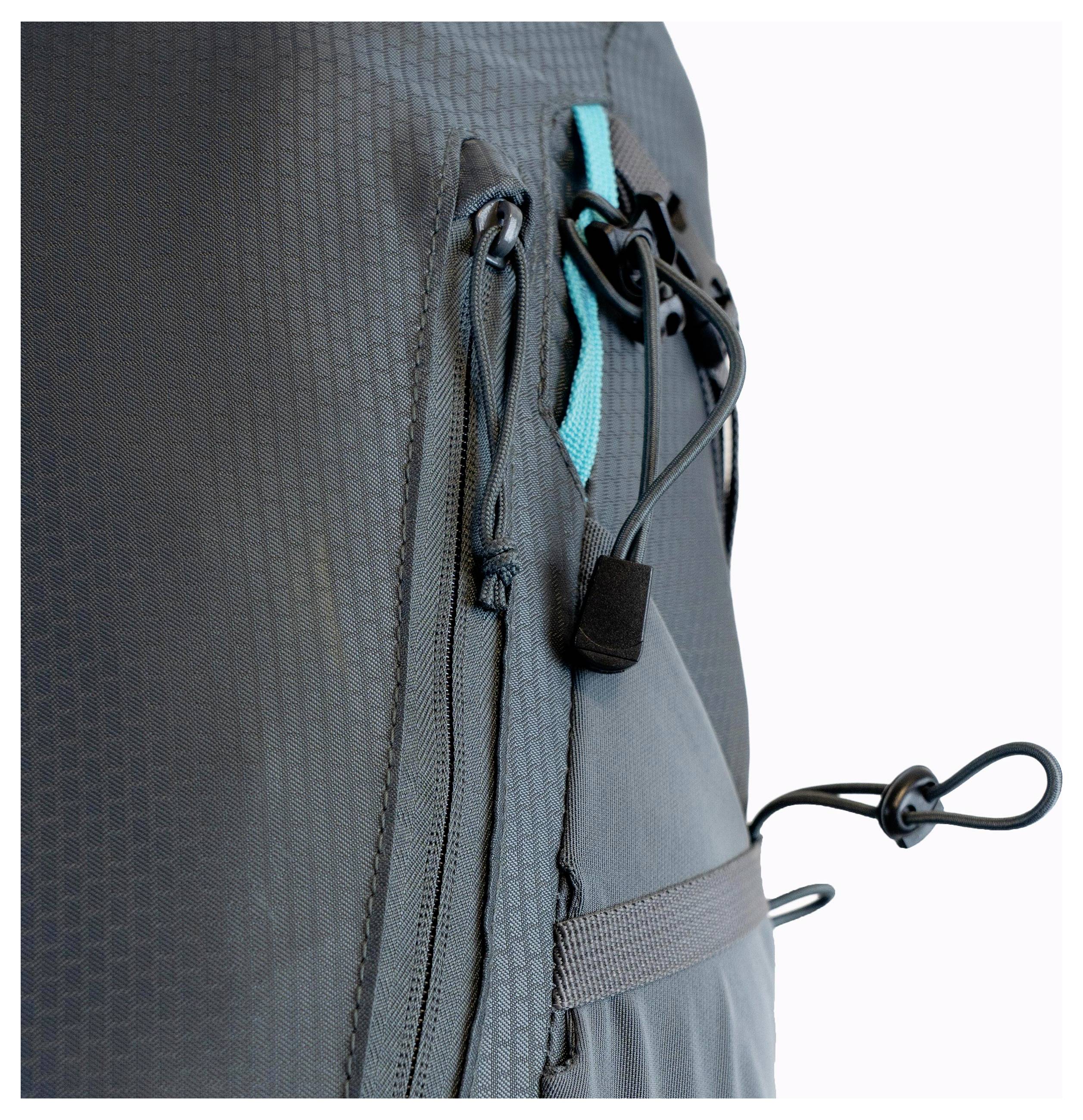 Eine Nahaufnahme eines Rucksacks aus strukturiertem dunklem Stoff mit einer blaugrünen Akzentfarbe, einer Reißverschlusstasche und einem Spannseil an der Seite zum Straffen.