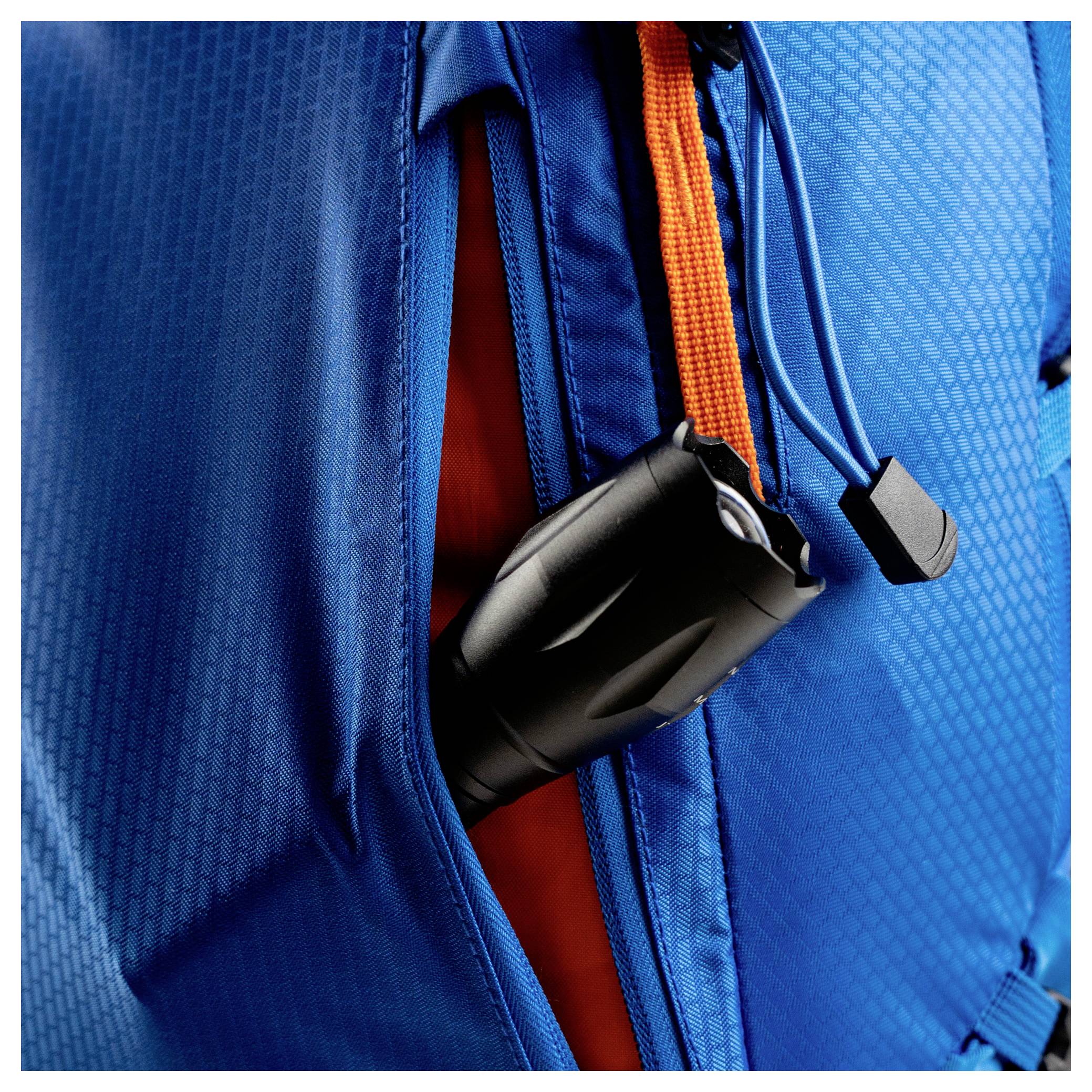 Eine schwarze Taschenlampe ist mit einem Clip an einem orangefarbenen Gurt in der Tasche eines blauen Rucksacks befestigt.
