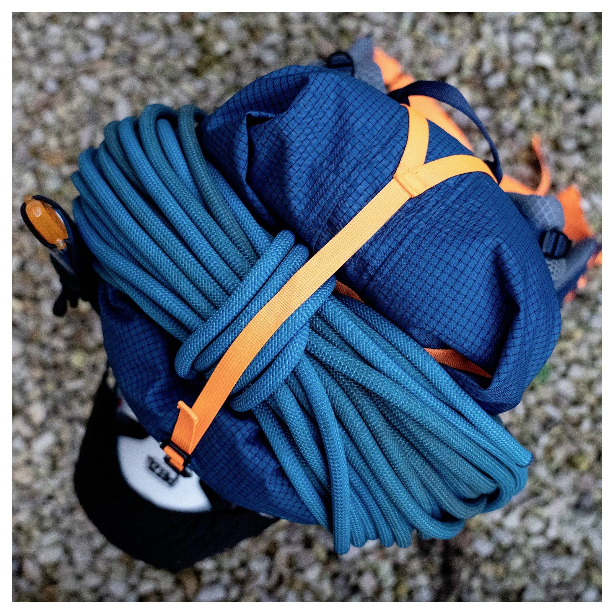 Ein Rucksack mit einem kompakten Kletterseil, das daran befestigt ist, von oben auf einer Kiesfläche betrachtet, was die Bereitschaft für ein Outdoor-Abenteuer andeutet.