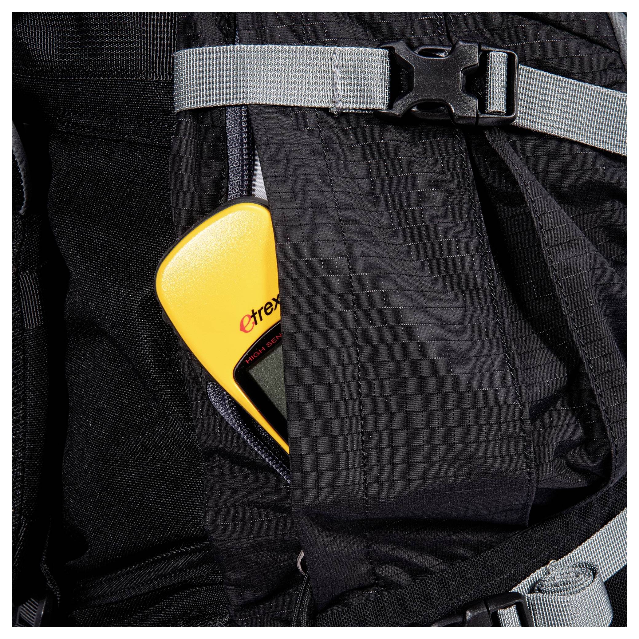 Ein gelbes GPS-Gerät, das teilweise in der Seitentasche eines schwarzen Rucksacks verstaut ist, mit grauen Riemen über der Tasche.