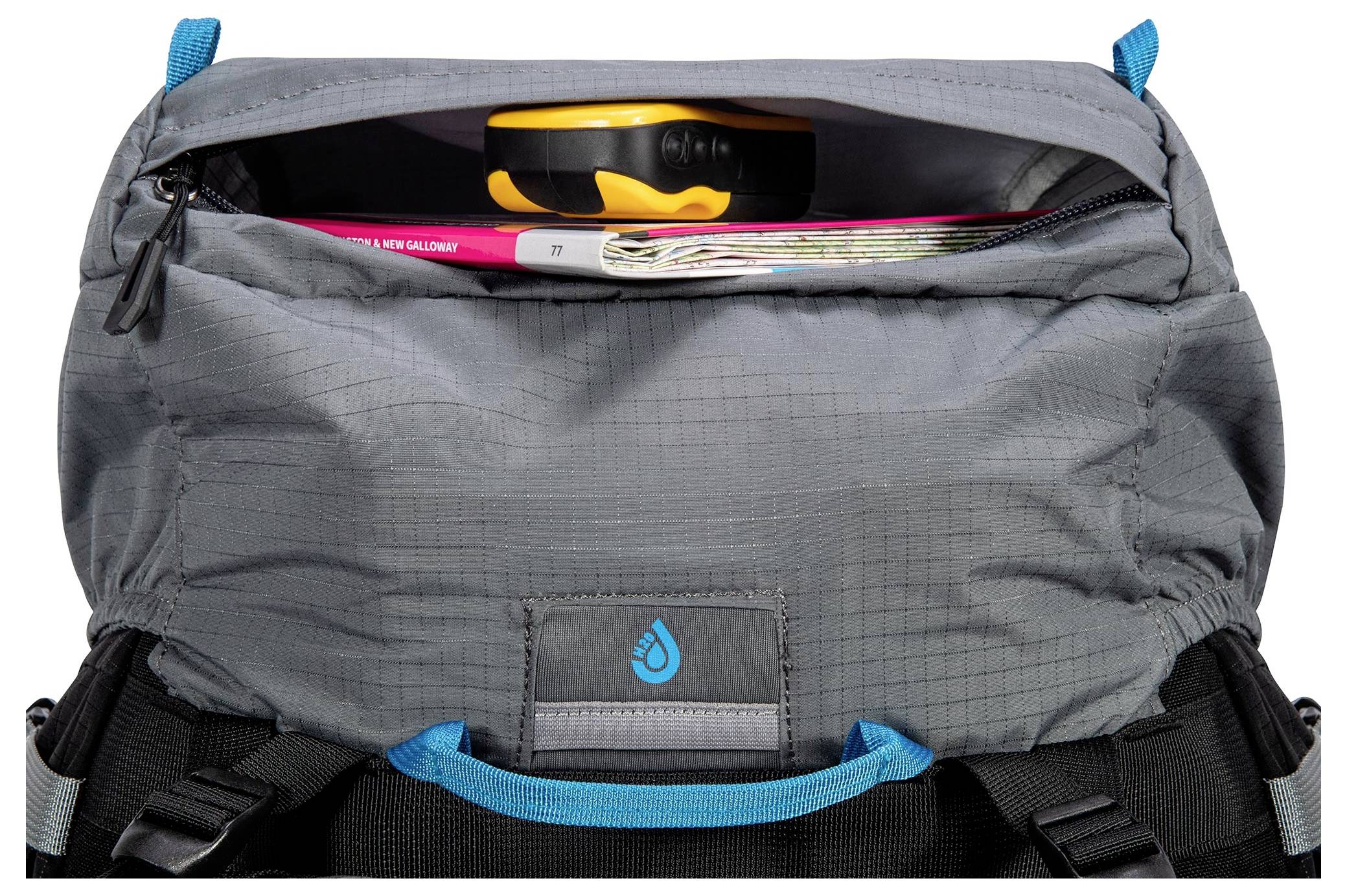 Ein grauer Rucksack mit einem offenen oberen Fach, das ein Stahllineal, eine aufgerollte Zeitschrift und eine Karte im Inneren zeigt.