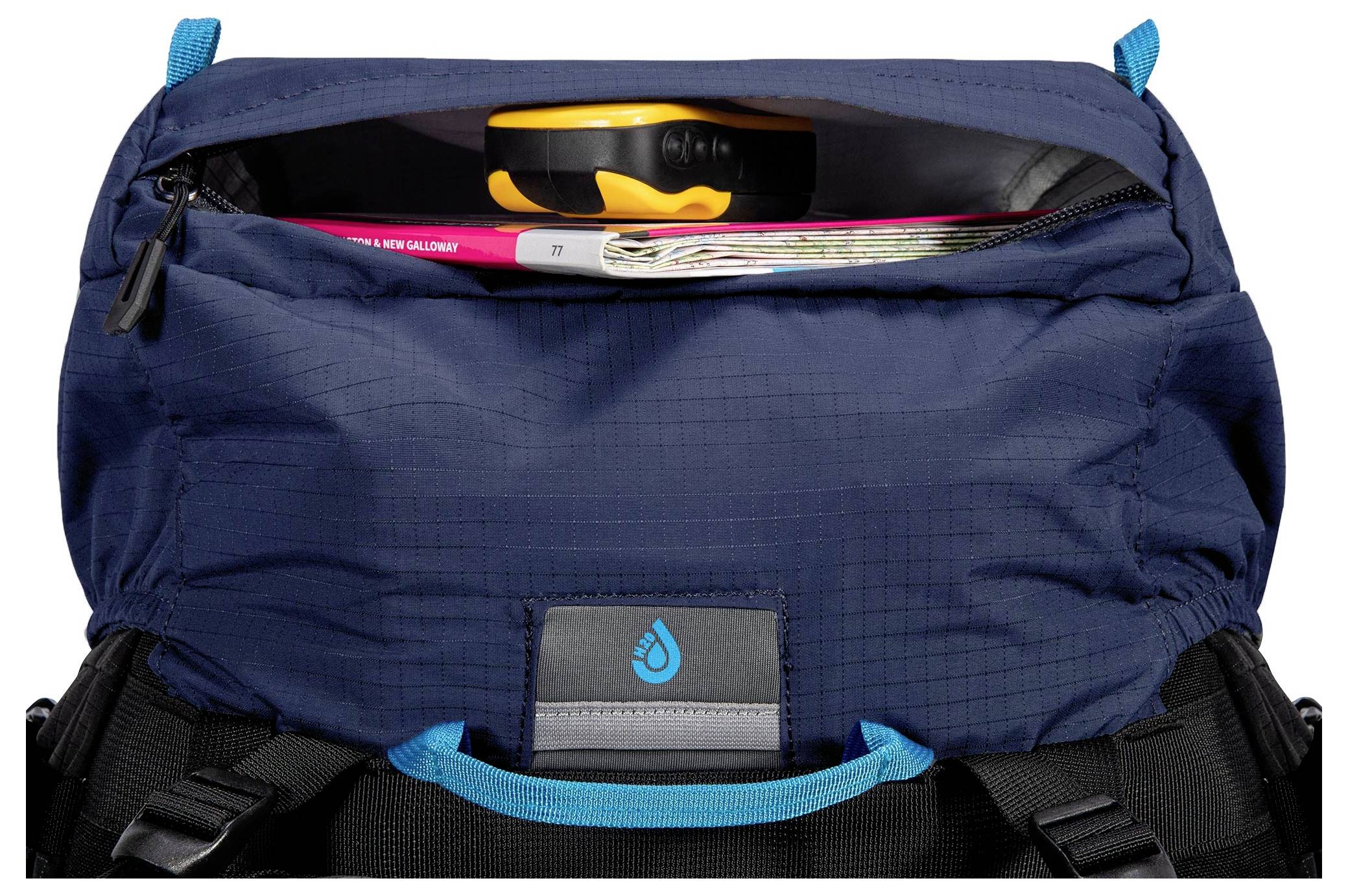 Ein Rucksackfach, das offen ist und ein Stahllineal und ein Magazin darin zeigt, mit einem Wassertropfen-Logo auf der Klappe, hauptsächlich blau mit schwarzen Riemen.