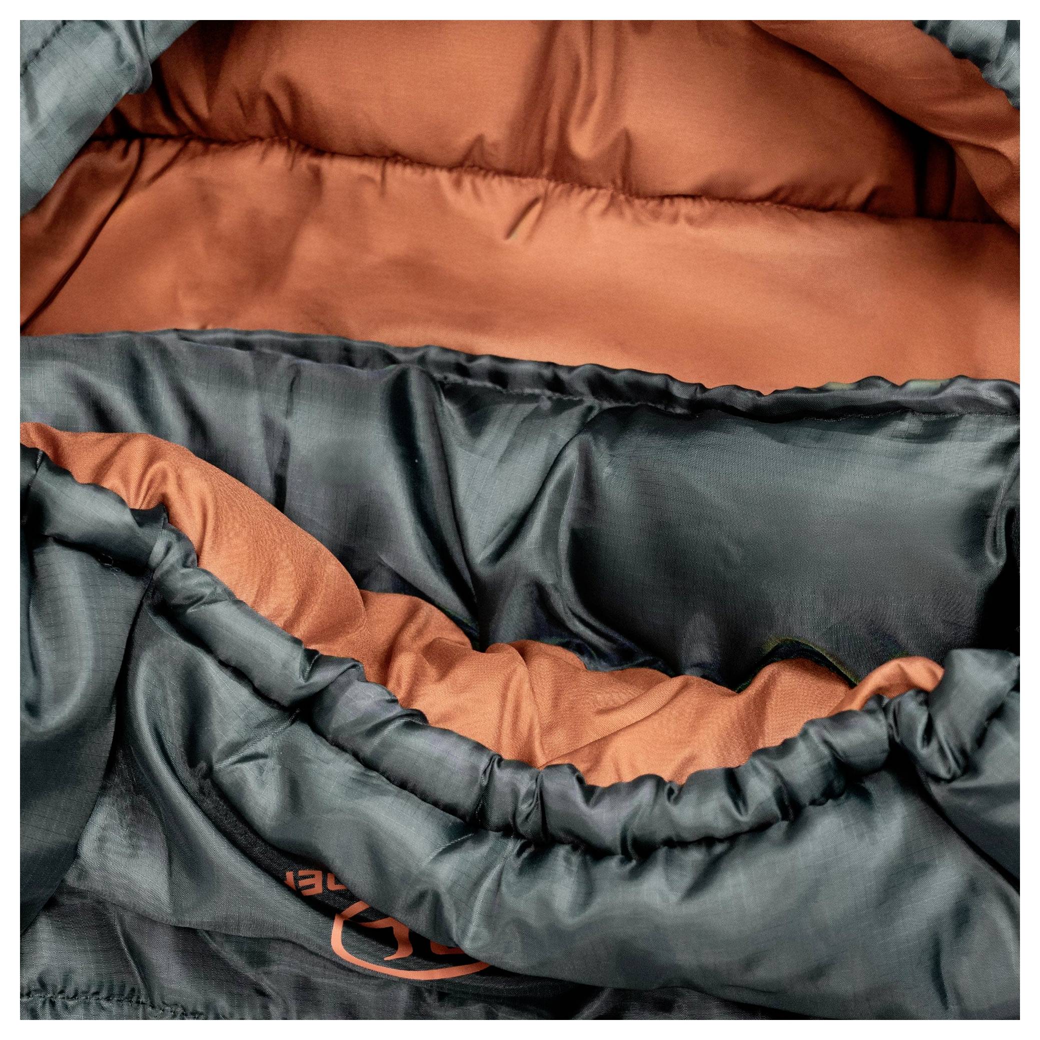 Nahaufnahme eines Schlafsacks mit weichem, orangefarbenem Innenfutter und dunkelgrünem Außenmaterial, das die Plüschauskleidung und Nähdetails zeigt.