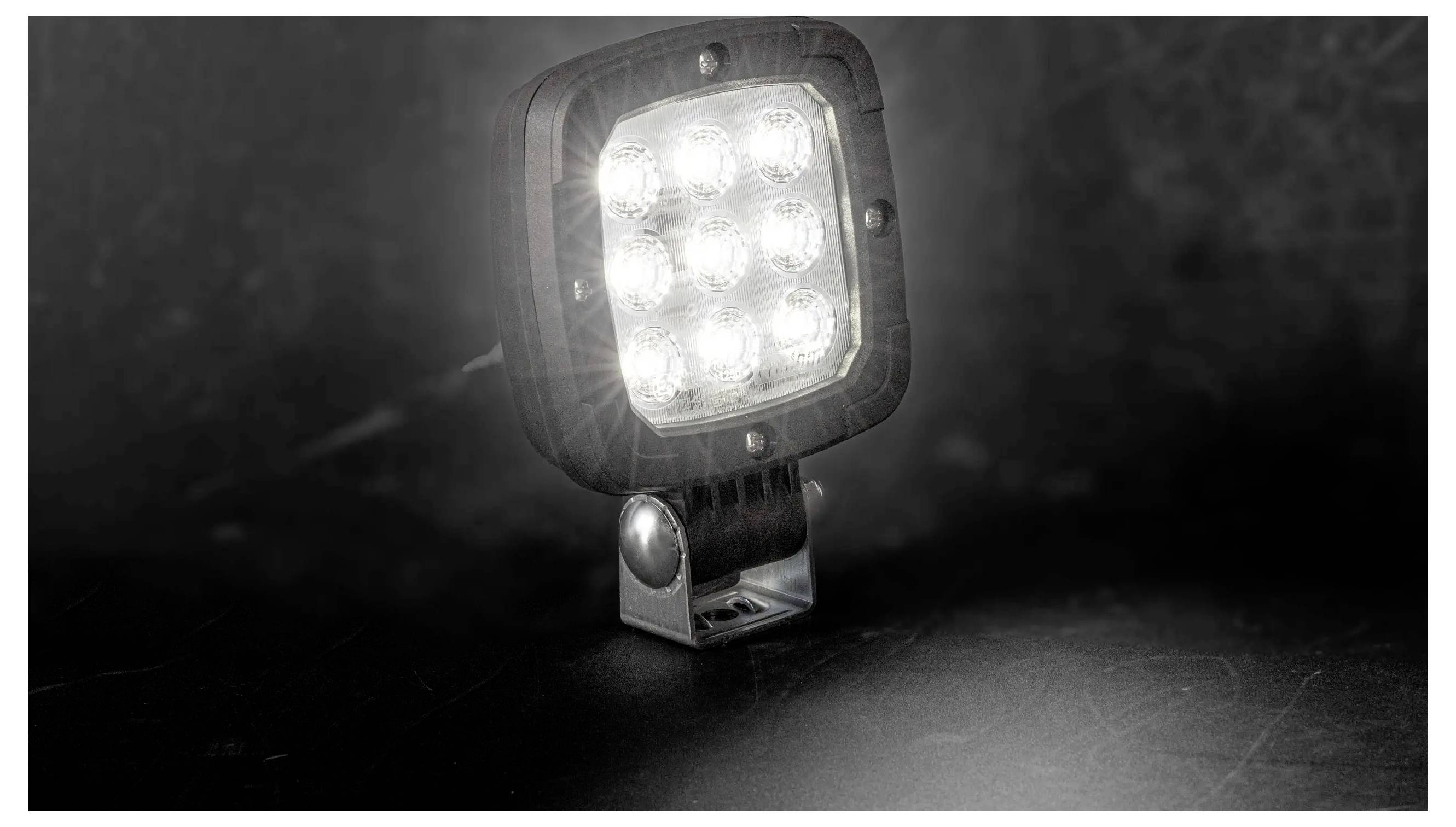 Helles LED-Arbeitslicht auf einer kleinen verstellbaren Halterung, leuchtend vor dunklem Hintergrund.