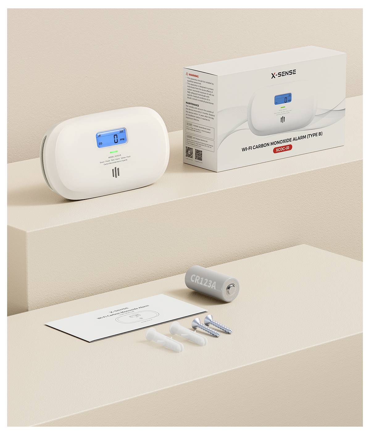 Ein CO-Melder mit Bedienungsanleitung, Batterie und Montagematerial auf einer cremefarbenen Oberfläche neben einer Verpackung.