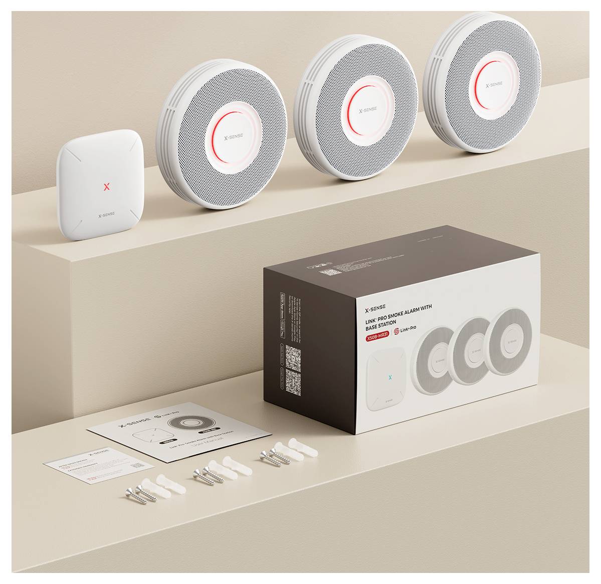 Paket mit drei runden Rauch- und Hitzemeldern, einem quadratischen Gerät, Schrauben und Anleitung, alle auf einer beigen Oberfläche platziert.
