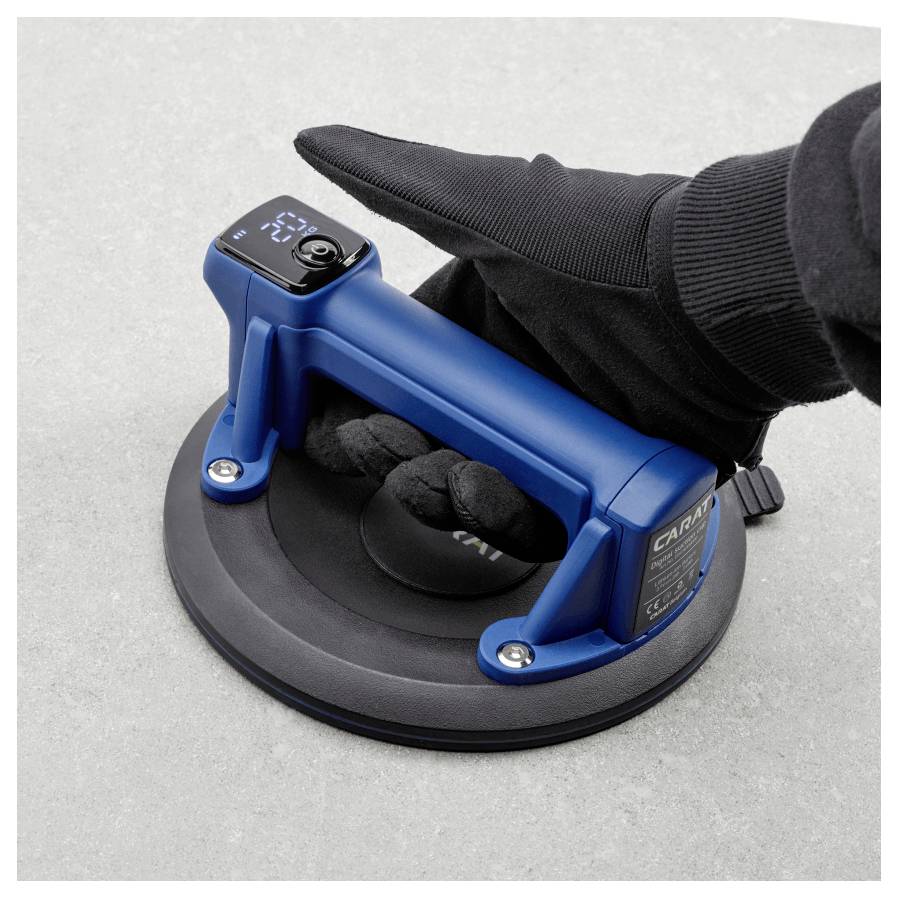 Eine behandschuhte Hand bedient einen blauen Vakuum-Saugnapf auf einer glatten grauen Oberfläche, wahrscheinlich zum sicheren und zuverlässigen Heben schwerer Objekte.