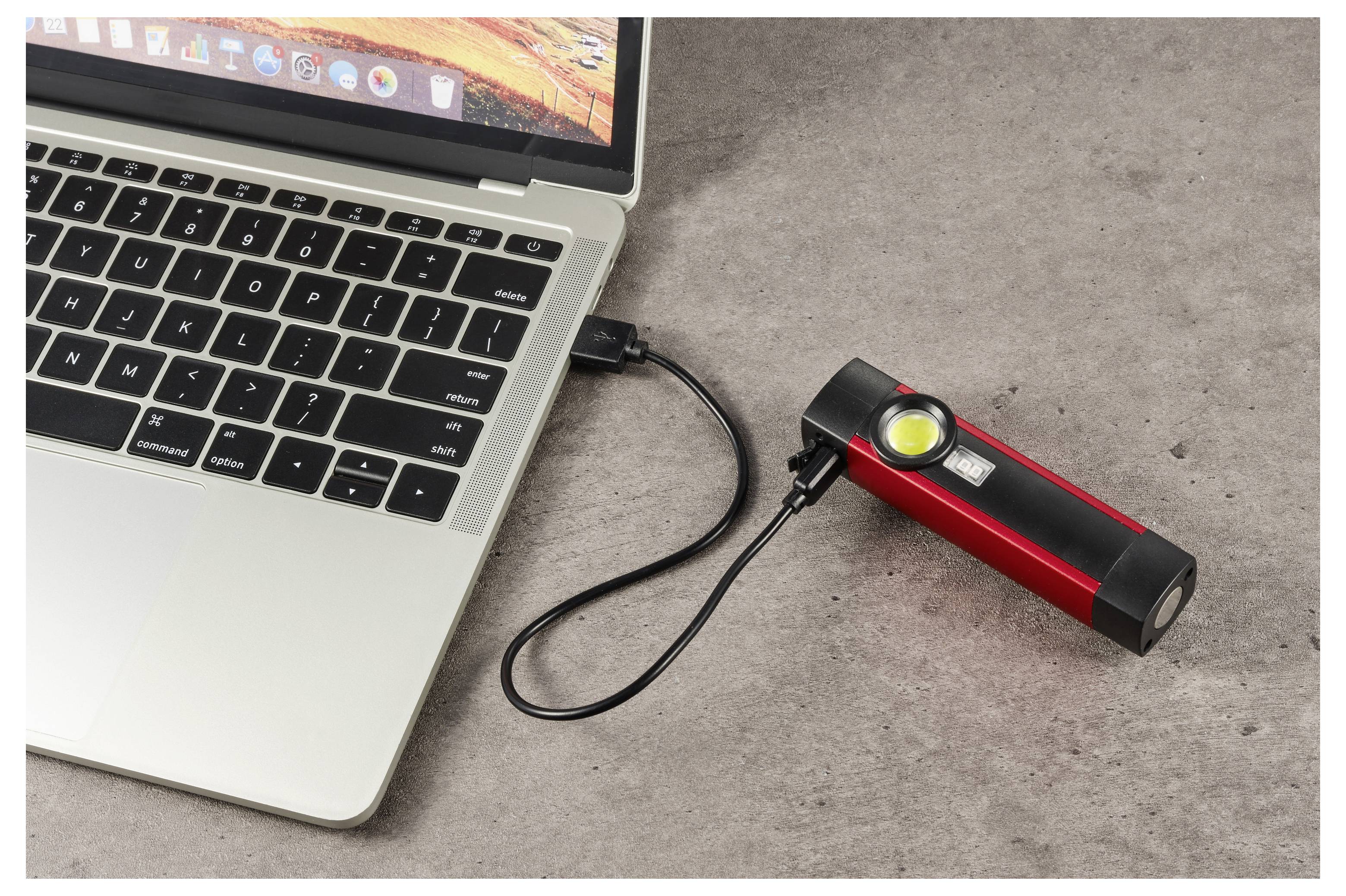 Laptop, der über ein USB-Kabel mit einer roten tragbaren Powerbank mit leuchtender Anzeigelampe auf einer Tischplatte verbunden ist.