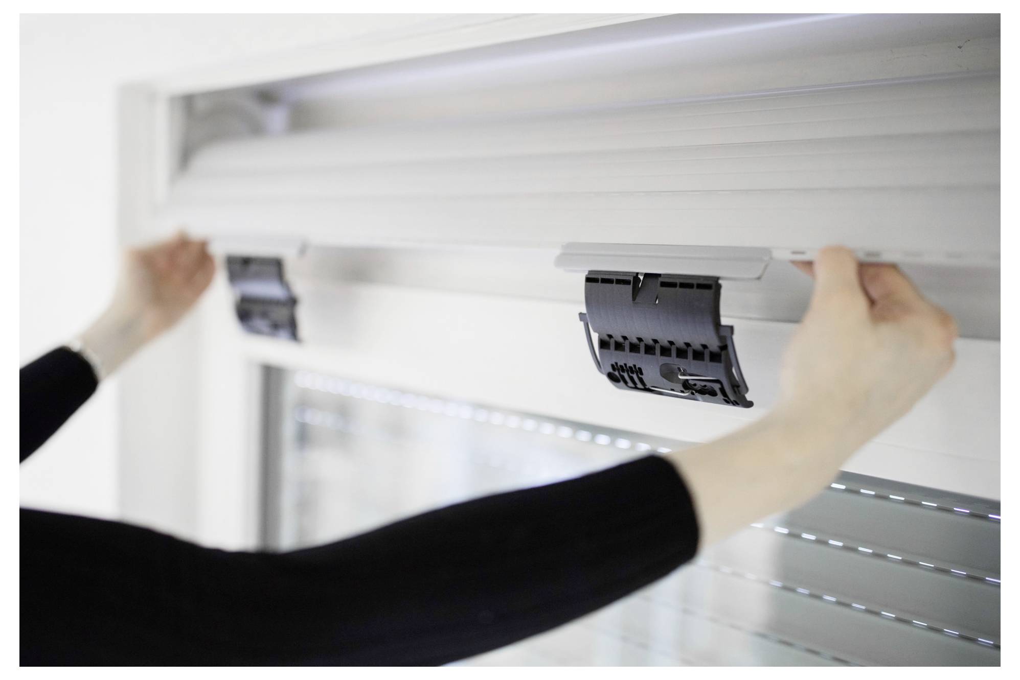 Person, die eine Rolllade am oberen Fensterbereich einstellt, zeigt den Mechanismus und die Position für Installation oder Wartung.