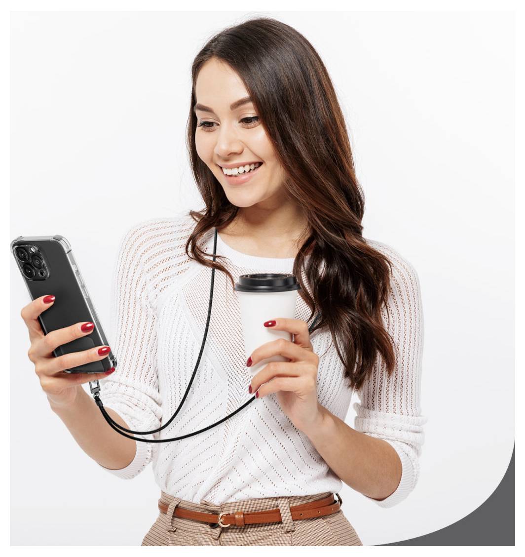 Eine lächelnde Frau hält ein Smartphone und einen Kaffeebecher zum Mitnehmen, trägt einen weißen Pullover und beige Hosen und schaut auf ihr Telefon.