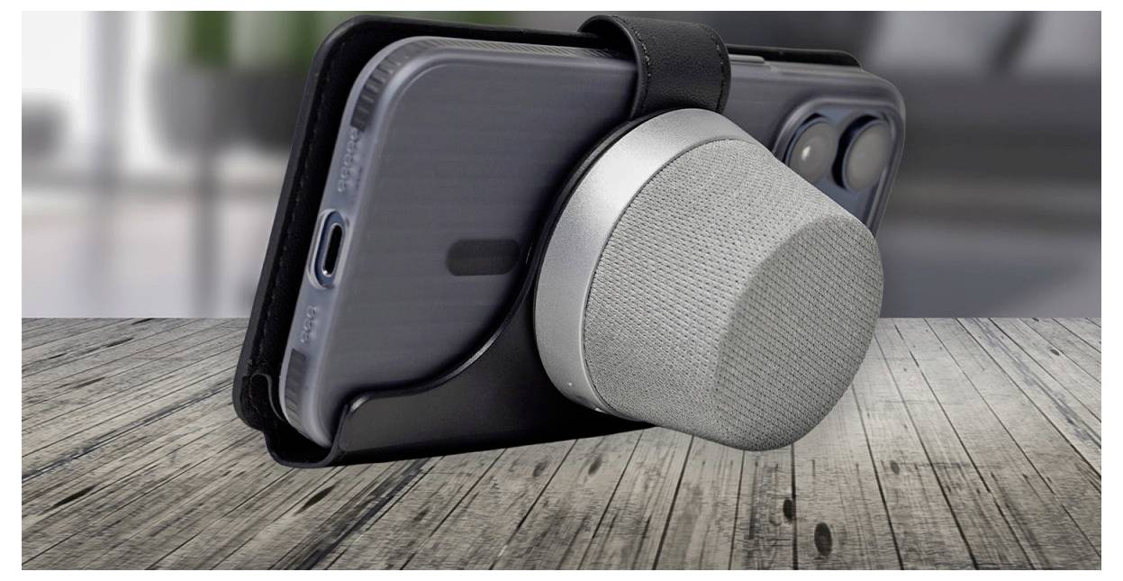 Ein Smartphone mit einem abnehmbaren kreisförmigen Lautsprecher, der auf der Rückseite befestigt ist, ruht auf einer Holzoberfläche in Innenräumen.