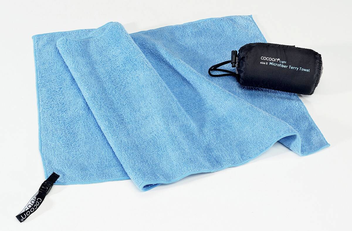 Ein weiches, blaues Microfaser-Frotteetuch ausgebreitet, neben einem kleinen, passenden Transportbeutel mit der Aufschrift „Cocoon-Microfaser-Frotteetuch