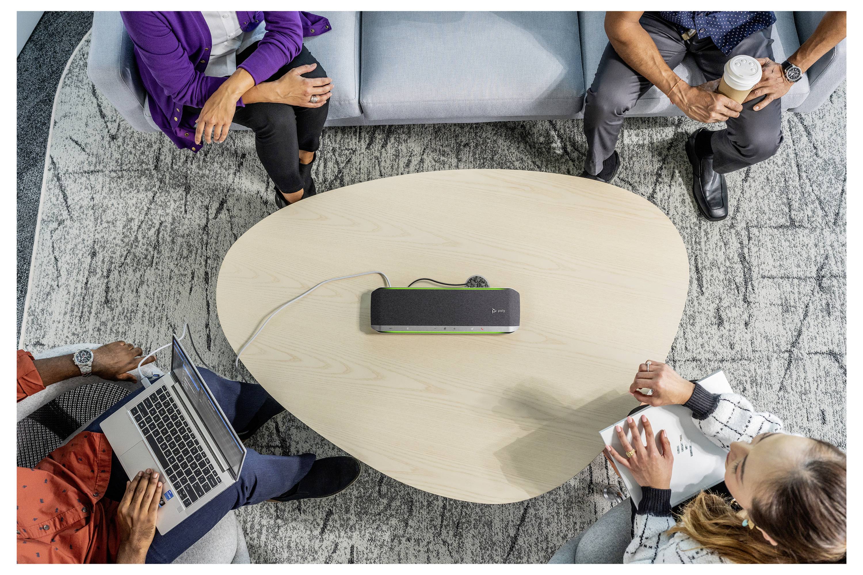 Vier Personen sitzen um einen ovalen Tisch und arbeiten zusammen mit Laptops und Notizbüchern. Ein Sprechergerät ist in der Mitte des Tisches platziert.