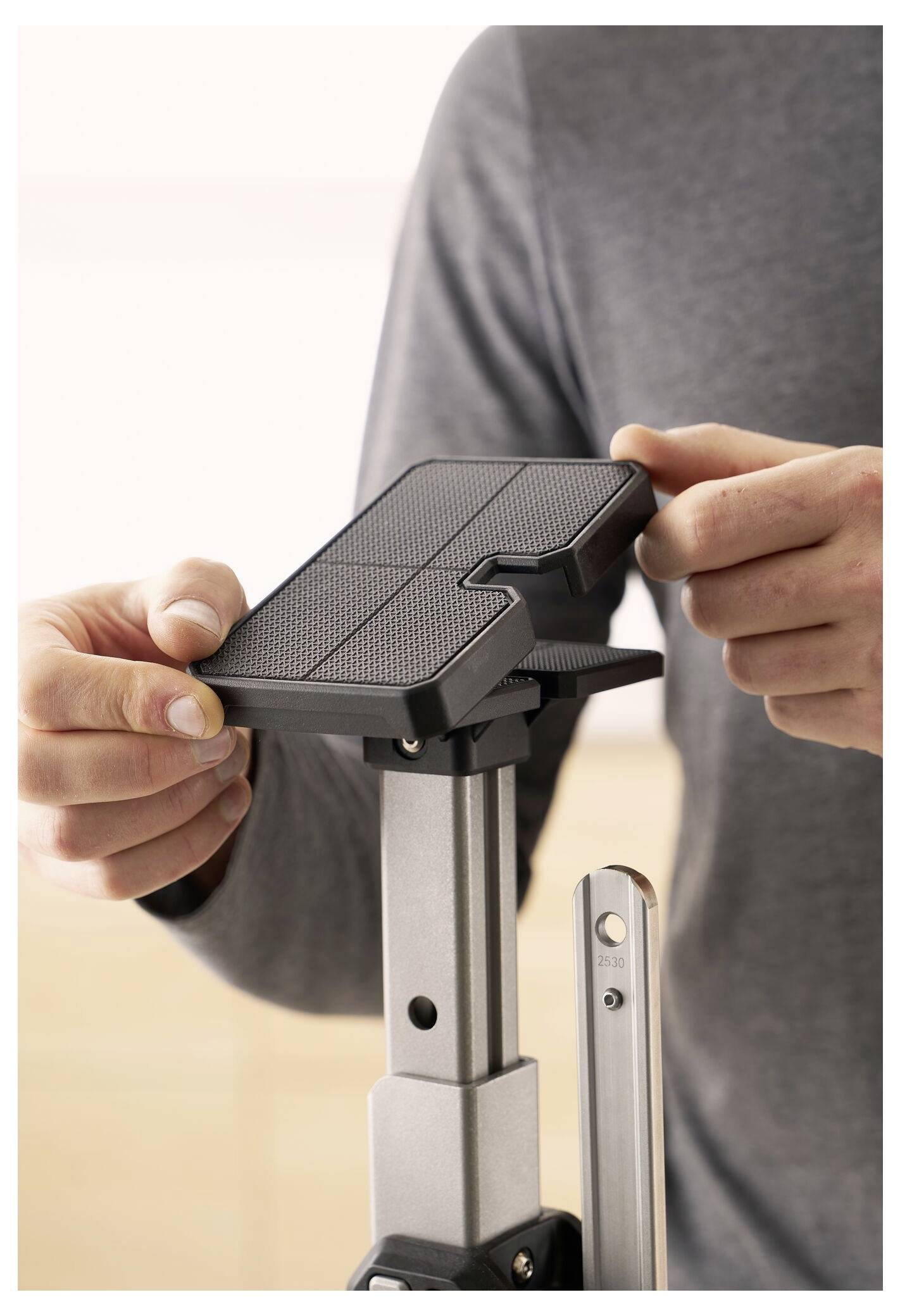 Eine Person stellt die Höhe eines Monitorständers ein, indem sie mit einer Hand einen Knopf an der Seite drückt und mit der anderen Hand die Plattform hält.