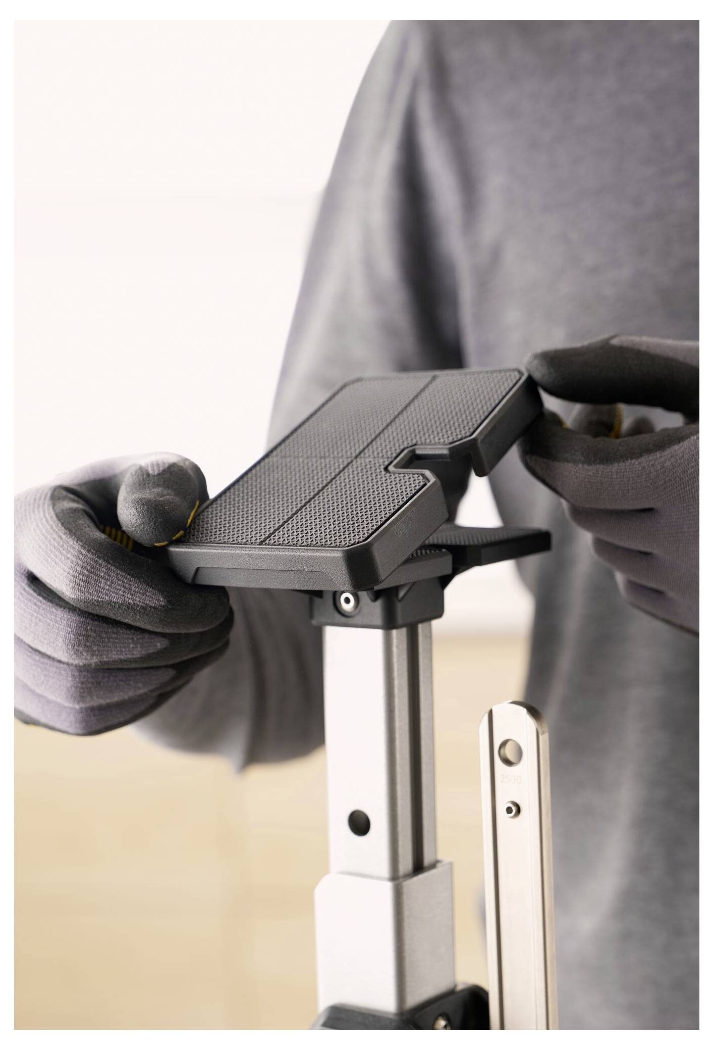 Eine Person mit Handschuhen stellt ein strukturiertes Gerät auf einem metallischen Ständer ein, was auf einen Fokus auf Präzisionsarbeit oder Montagearbeiten hindeutet.