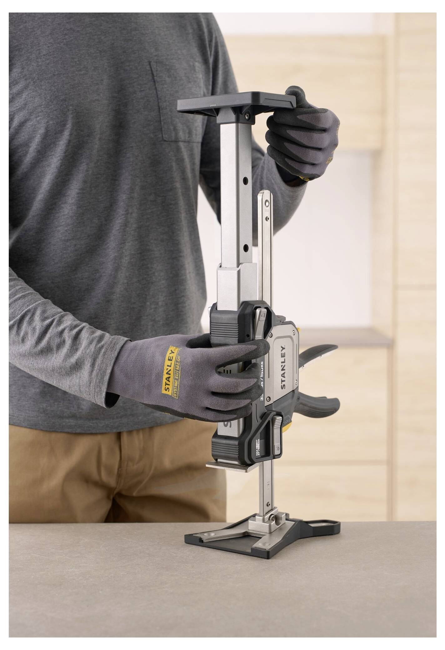 Eine Person mit Handschuhen stellt eine Metallzwinge auf einer Tischplatte ein und demonstriert deren Verwendung in einer Schreinerei oder im Bauwesen.