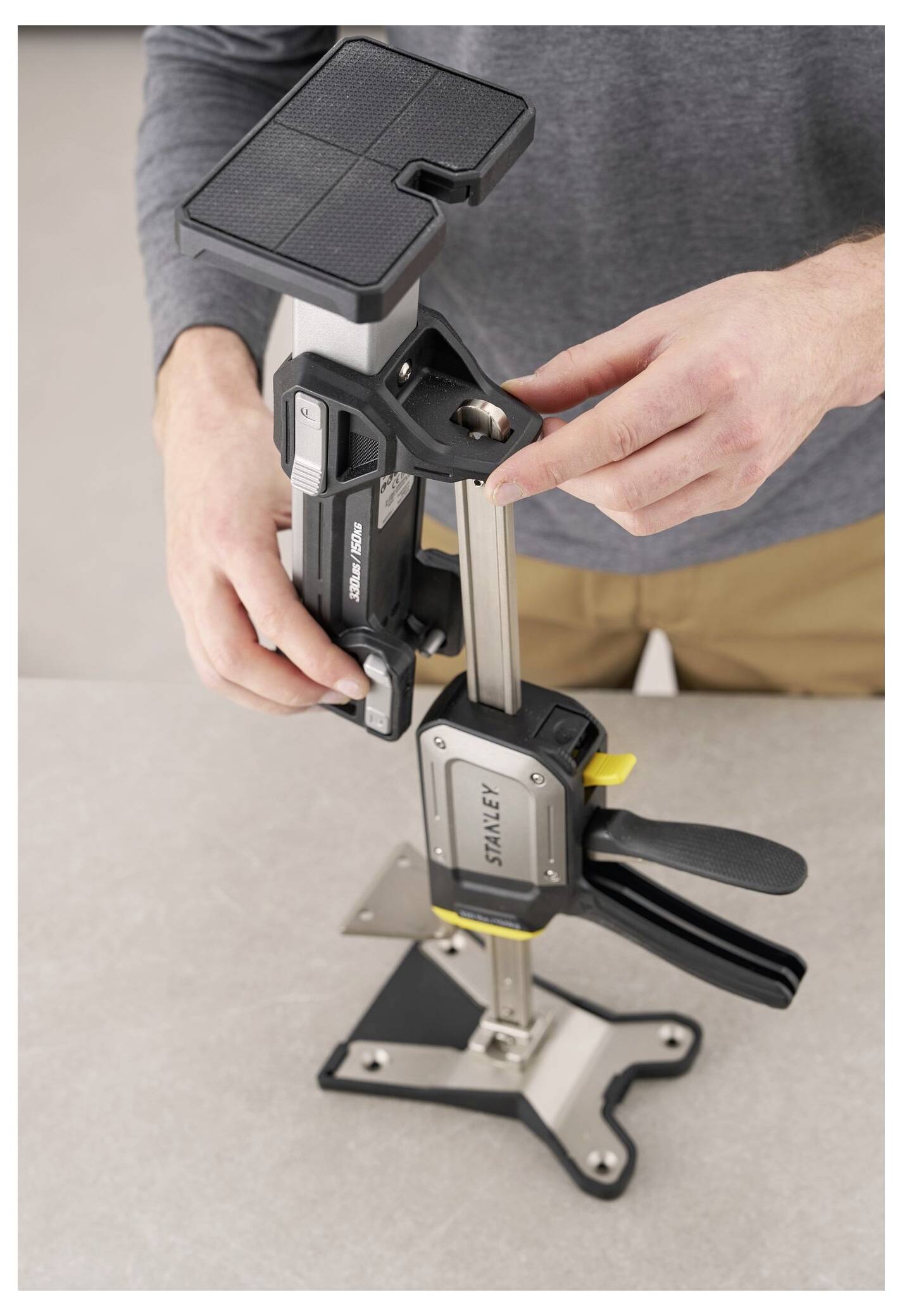 Eine Person stellt einen Stanley-Ständer auf einer Arbeitsplatte ein und demonstriert, wie man den verstellbaren Mechanismus zum Halten und Sichern von Werkzeugen verwendet.