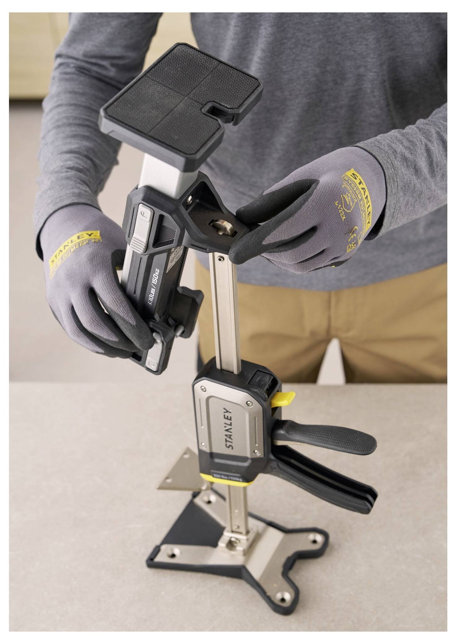 Eine Person stellt ein Spannwerkzeug auf einer Werkbank ein und demonstriert dessen Verwendung. Der Fokus liegt auf dem Mechanismus des Werkzeugs und dem Griff.