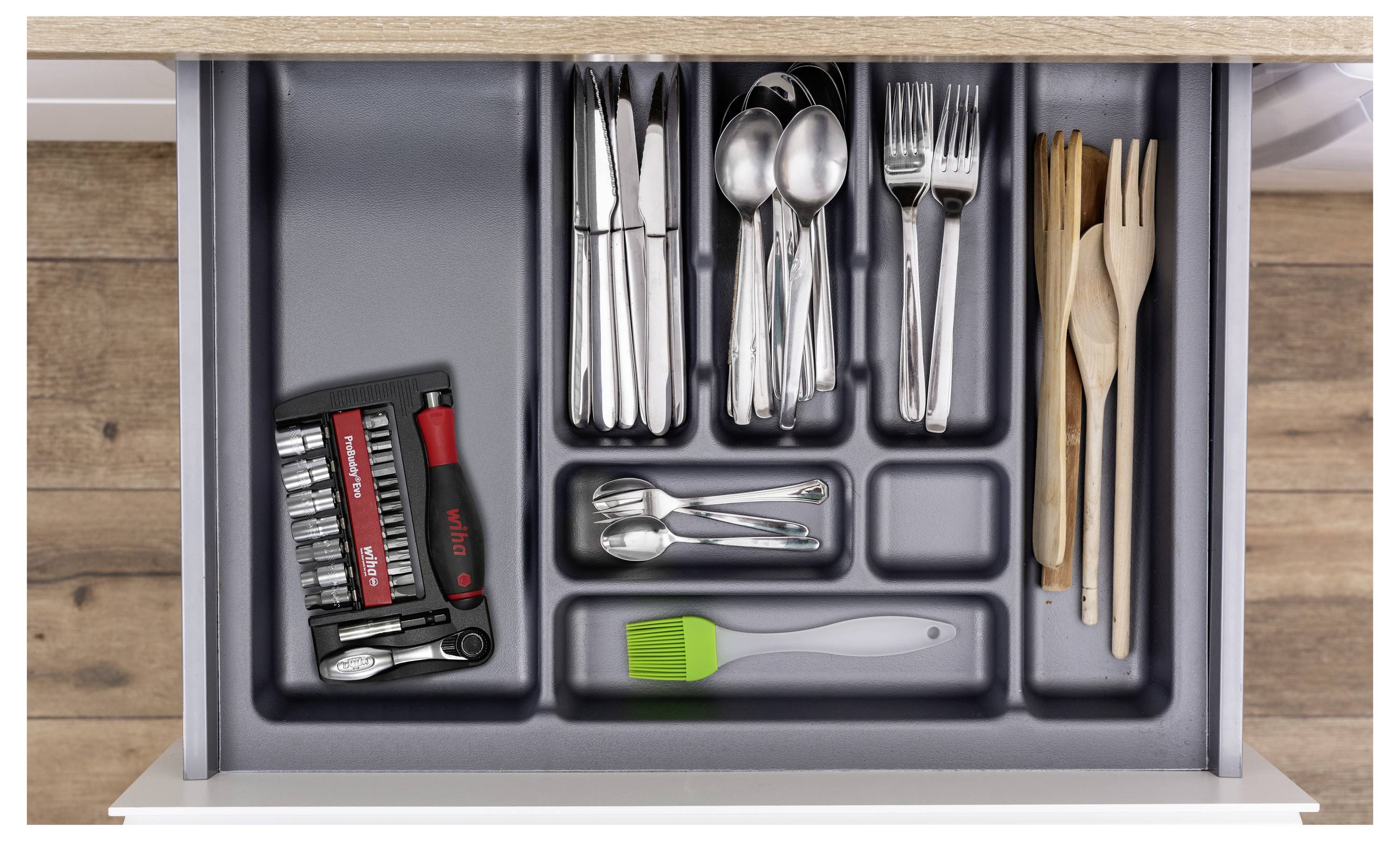 Offene Schublade mit organisierten Utensilien: Besteck in Fächern, ein kleines Werkzeugset auf der linken Seite und hölzerne Utensilien auf der rechten Seite.