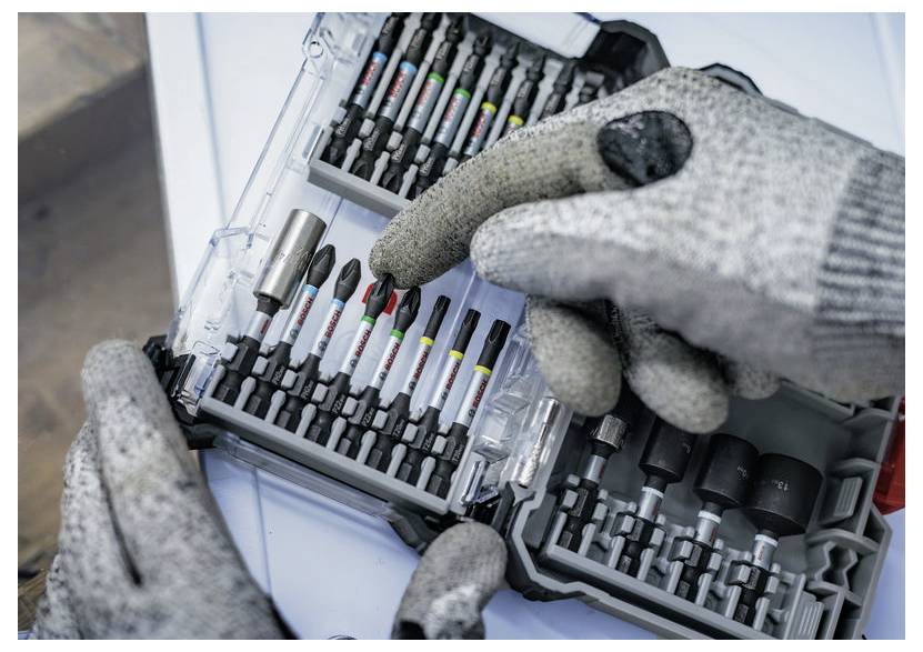 Eine Person mit grauen Handschuhen wählt einen Bohrer aus einem organisierten Set in einem transparenten Behälter aus und hebt damit Präzision und Sorgfalt hervor.