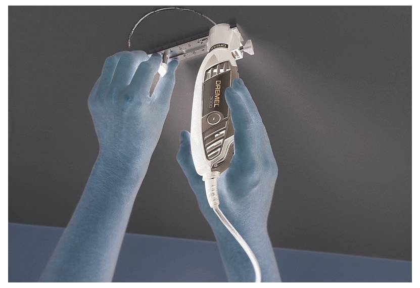 Eine Person benutzt ein Dremel-Werkzeug, um ein rundes Loch in die Decke zu schneiden, wobei sie eine Messlehre hält, um Präzision zu gewährleisten.