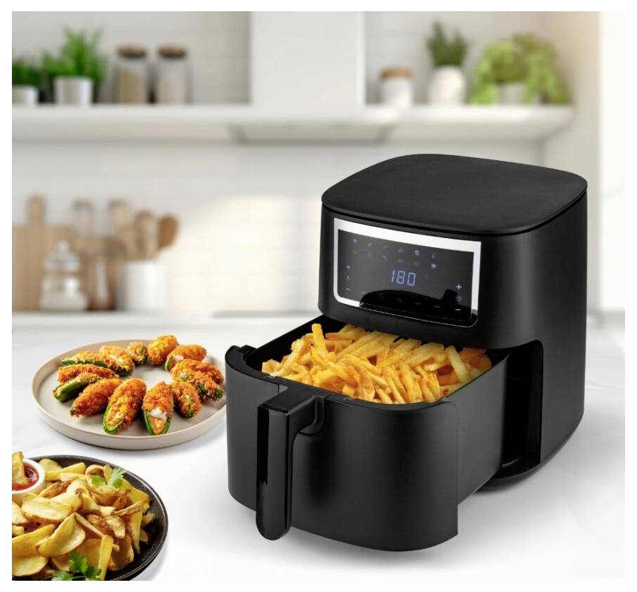 Ein Heißluftfriteuse auf einer Küchenarbeitsplatte mit einer Schublade voller Pommes und Tellern mit gekochtem Essen dahinter.