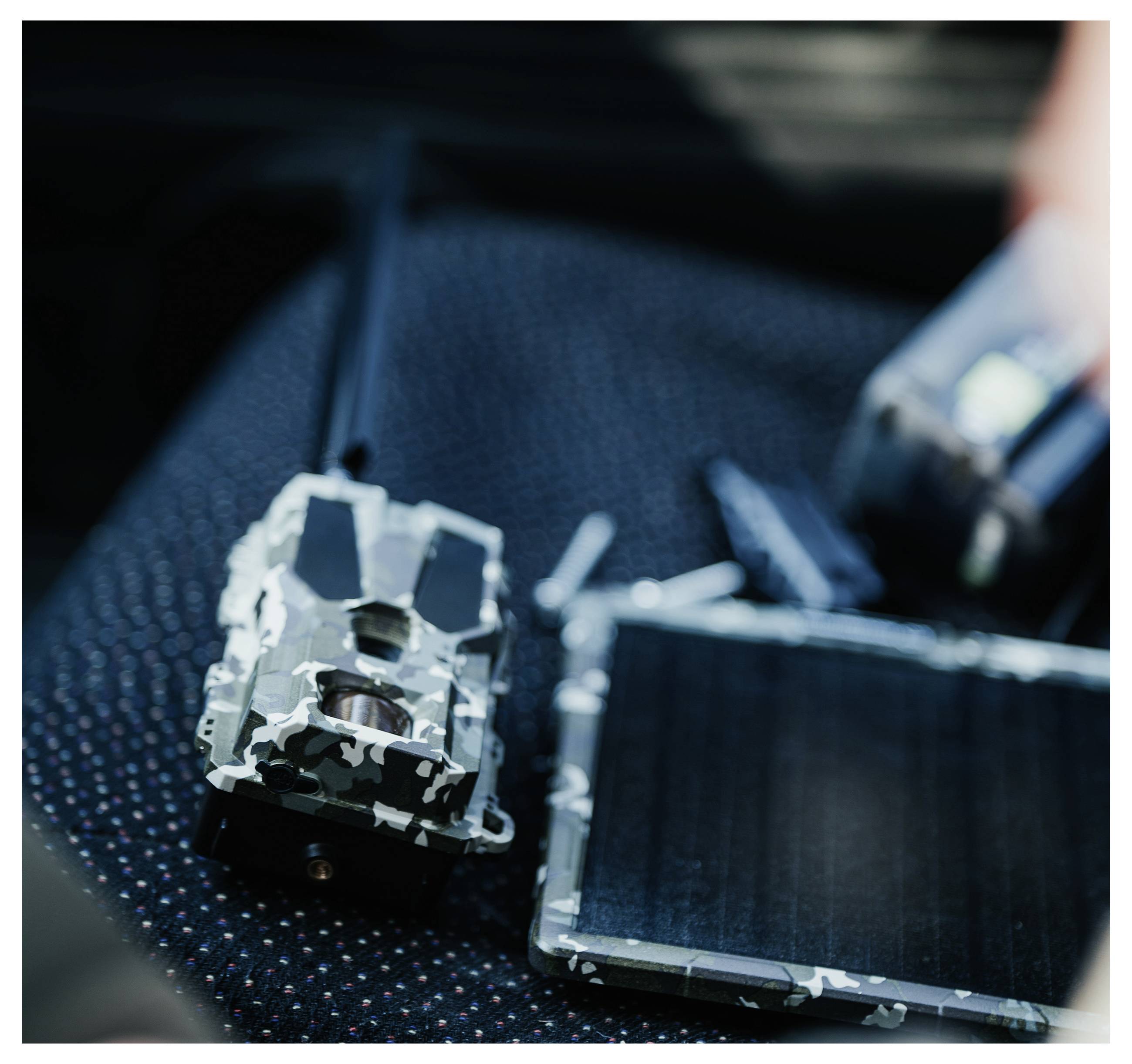 Ein getarnter Fernbedienung mit einer Antenne und einem Solarmodulgerät wird auf einer dunklen, strukturierten Oberfläche platziert, was auf militärische Verwendung hindeutet.