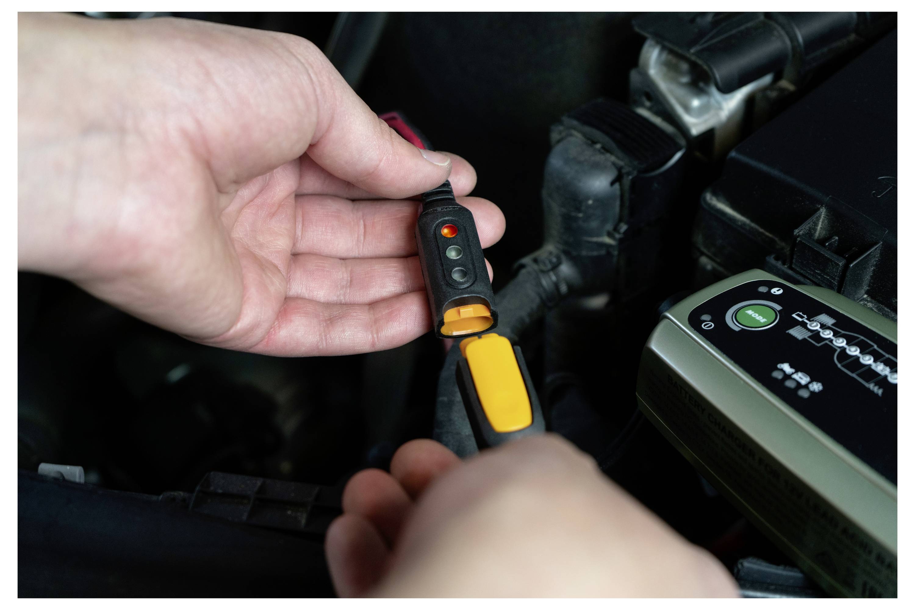 Eine Person, die einen Spannungsprüfer im Motorraum eines Autos verwendet, um elektrische Verbindungen zu überprüfen.