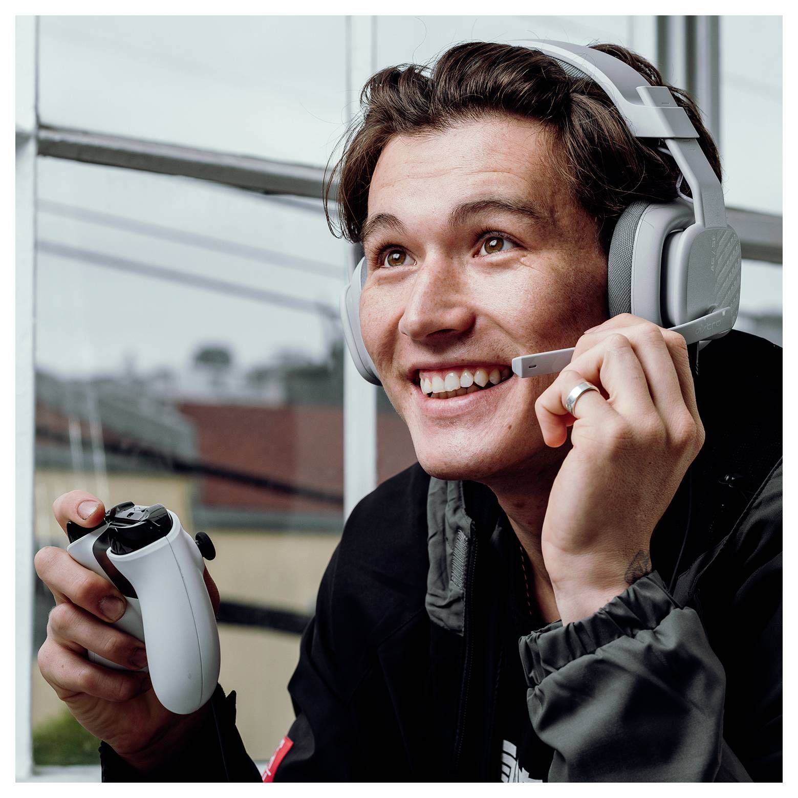 Lächelnder Gamer mit einem Kopfhörer, der einen Spielcontroller hält und während des Spiels ins Mikrofon spricht.