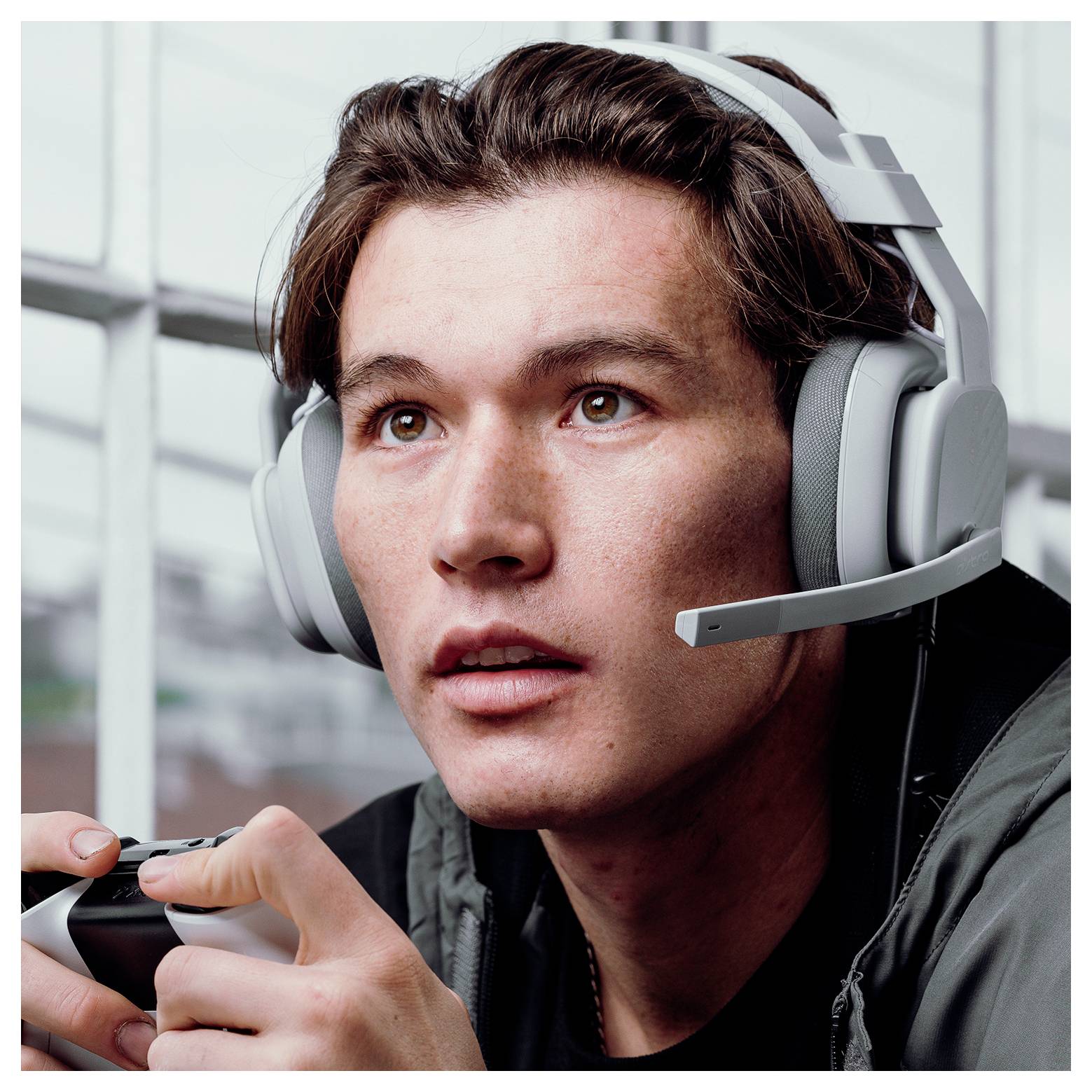 Junger Mann, der ein Gaming-Headset trägt, konzentriert sich, während er einen Controller hält und vermutlich ein Videospiel spielt.