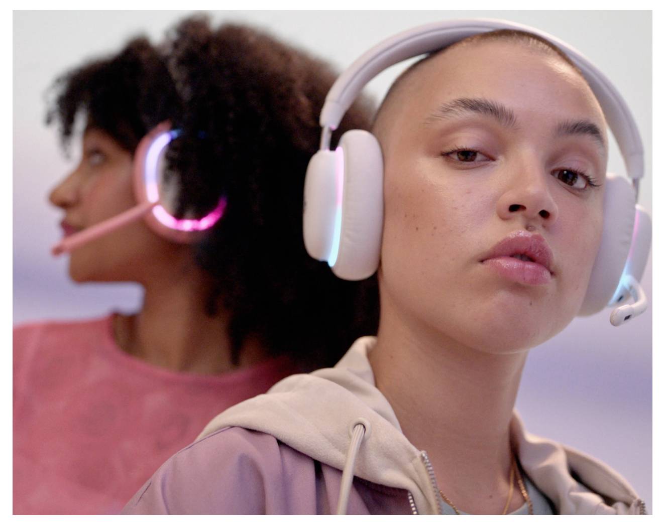 Zwei Frauen mit Gaming-Headsets, eine im Vordergrund blickt in die Kamera und eine unscharfe im Hintergrund schaut weg.